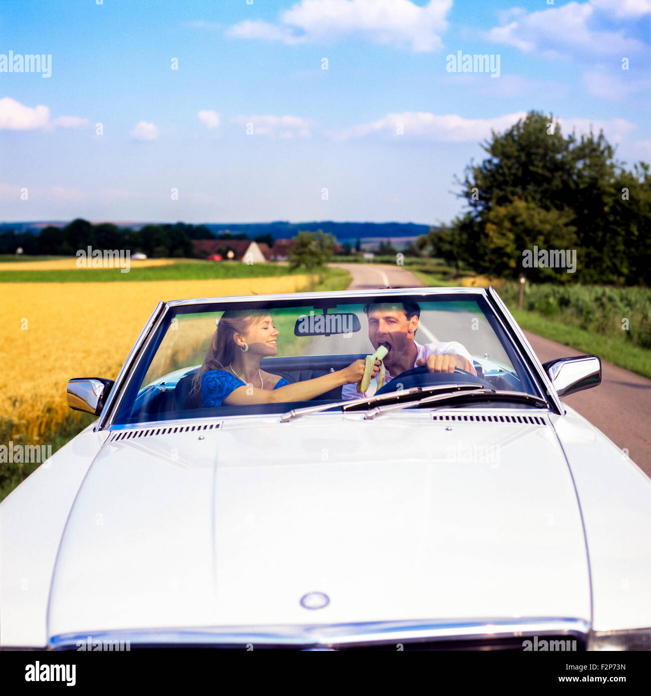 Frau Fütterung der Fahrer mit einer Banane während der Fahrt in einem Mercedes cabrio Auto auf Landstraße, Elsass, Frankreich, Europa Stockfoto