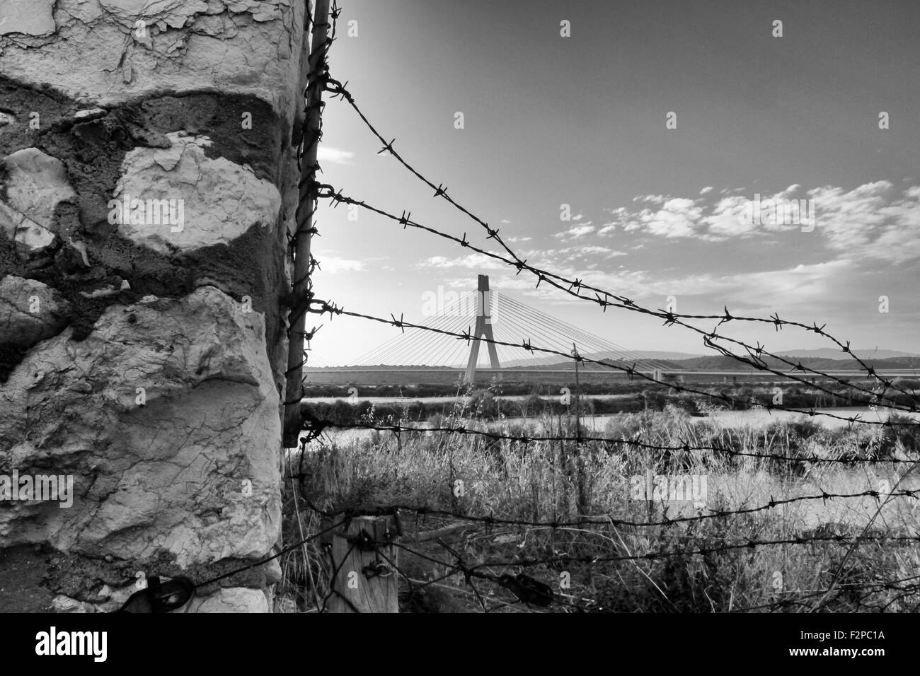 BW-Foto von einer Steinmauer mit Stacheldraht mit Brücke im Rücken Stockfoto BW-Foto von einer Steinmauer mit Stacheldraht mit Brücke im Rücken Stockfoto