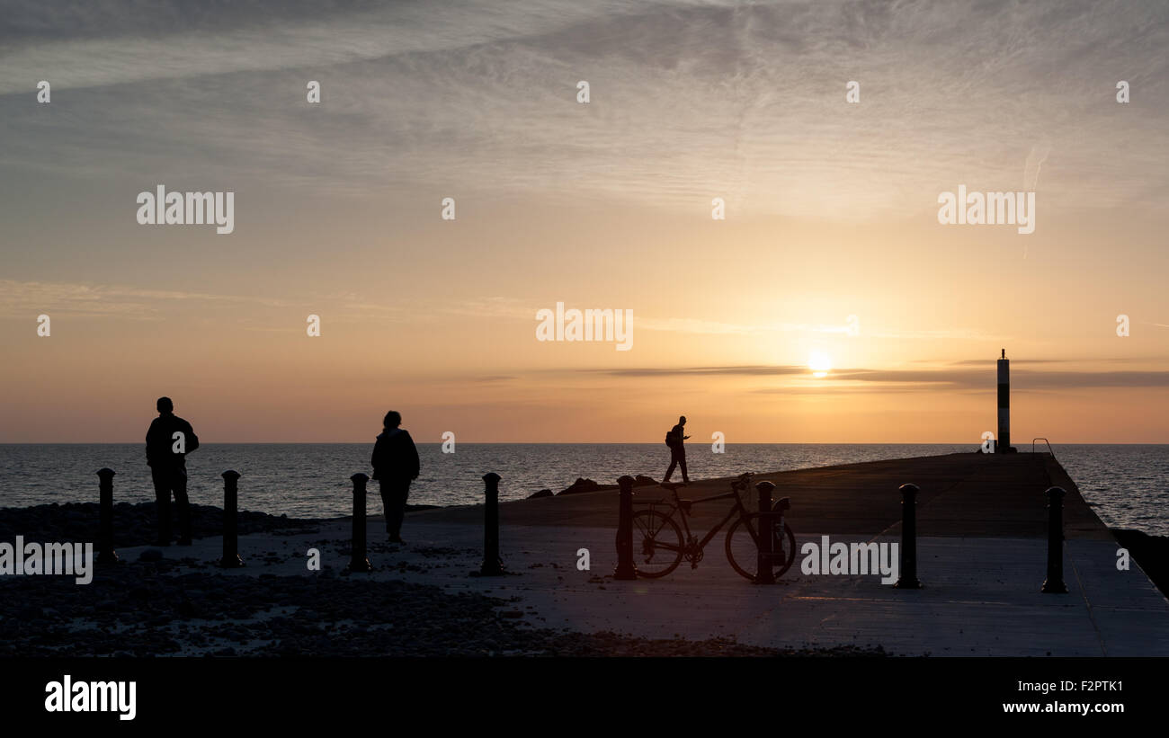 3 Personen und ein Fahrrad gegen einen schönen Sonnenuntergang bei Aberystwyth Stockfoto