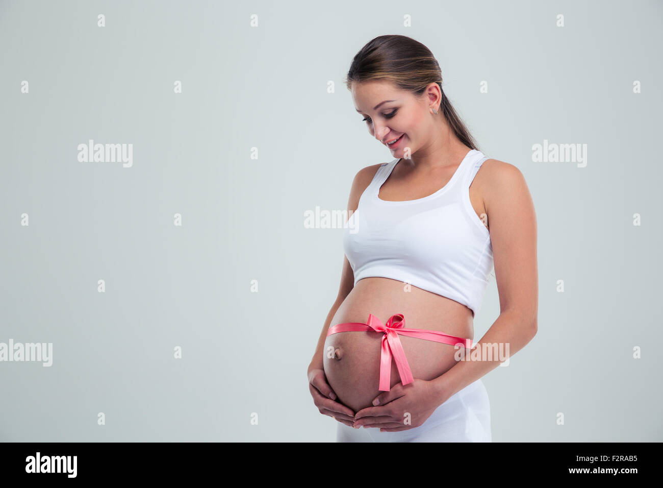 Porträt einer glücklich schwanger Frau streichelt ihren Bauch mit Geschenkband isoliert auf weißem Hintergrund Stockfoto