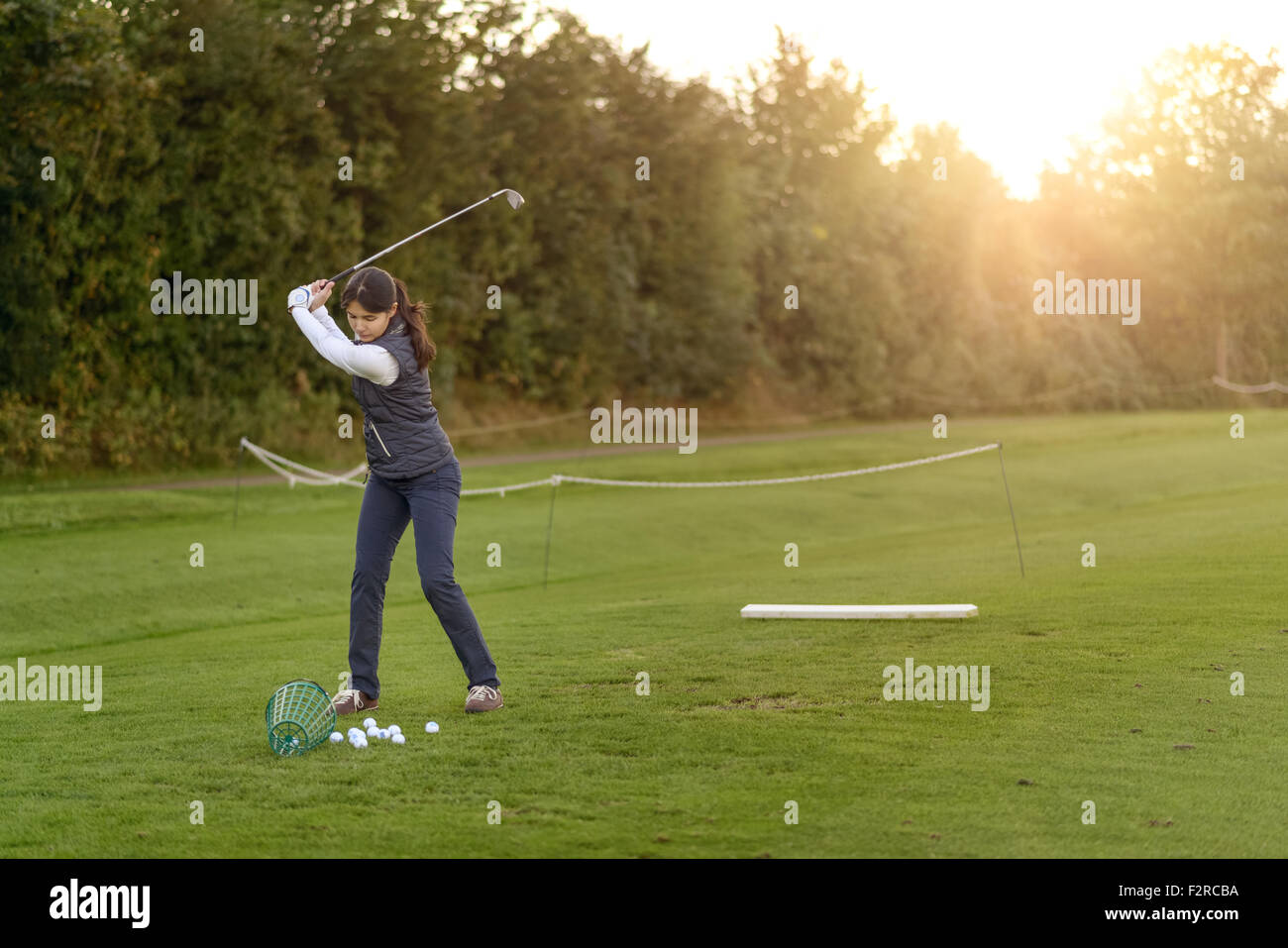 Golfspielerin stehend auf der driving Range am späten Nachmittag am Tag, während des Swingens konzentrieren ihr club Stockfoto