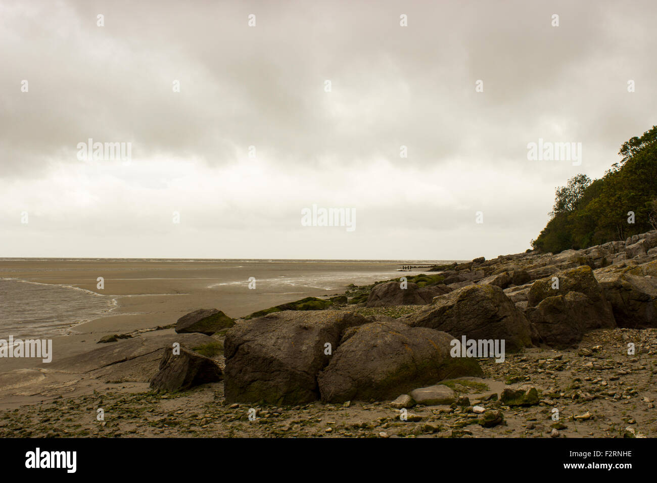 Das Meer in Morecambe Bay. Felsen am Strand, der über das Meer mit einem wolkigen Himmel schwebt über der Szene sieht. Stockfoto