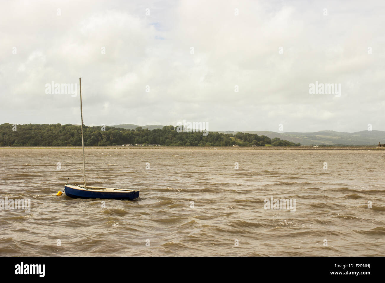 Das Meer in Morecambe Bay. Ein kleines blaues Boot segelt im Meer mit einem wolkigen Himmel schwebt über der Szene. Stockfoto