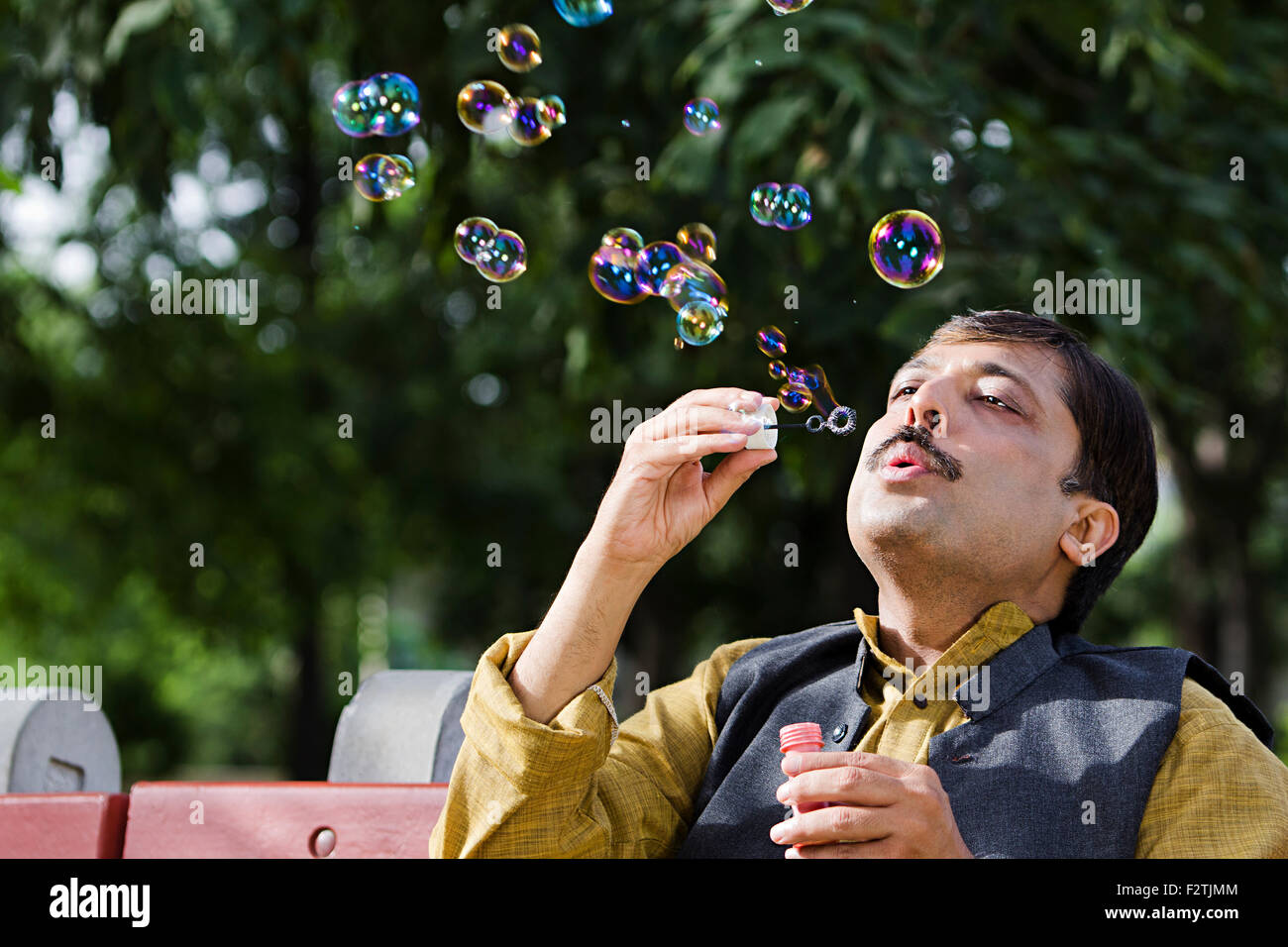 1 indische erwachsenen Mannes Park sitzen Bank spielen Bubble Zauberstab Stockfoto