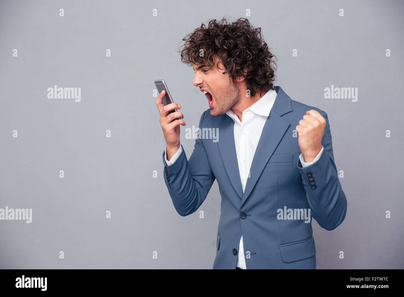 Porträt von wütenden Geschäftsmann schreien auf Smartphone über grauen Hintergrund Stockfoto