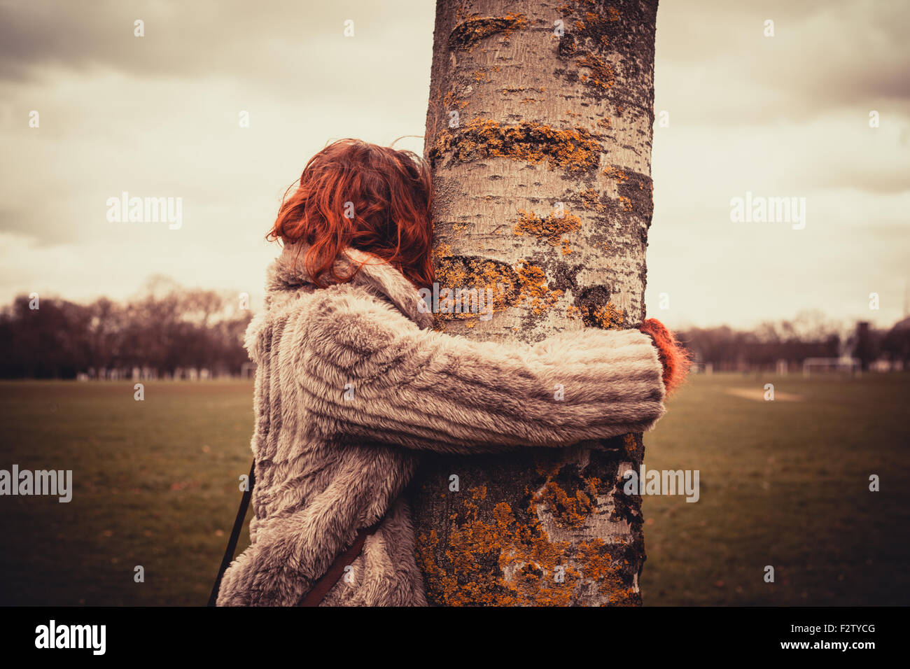 Junge Frau im Park an einem Wintertag und umarmt einen Baum Stockfoto