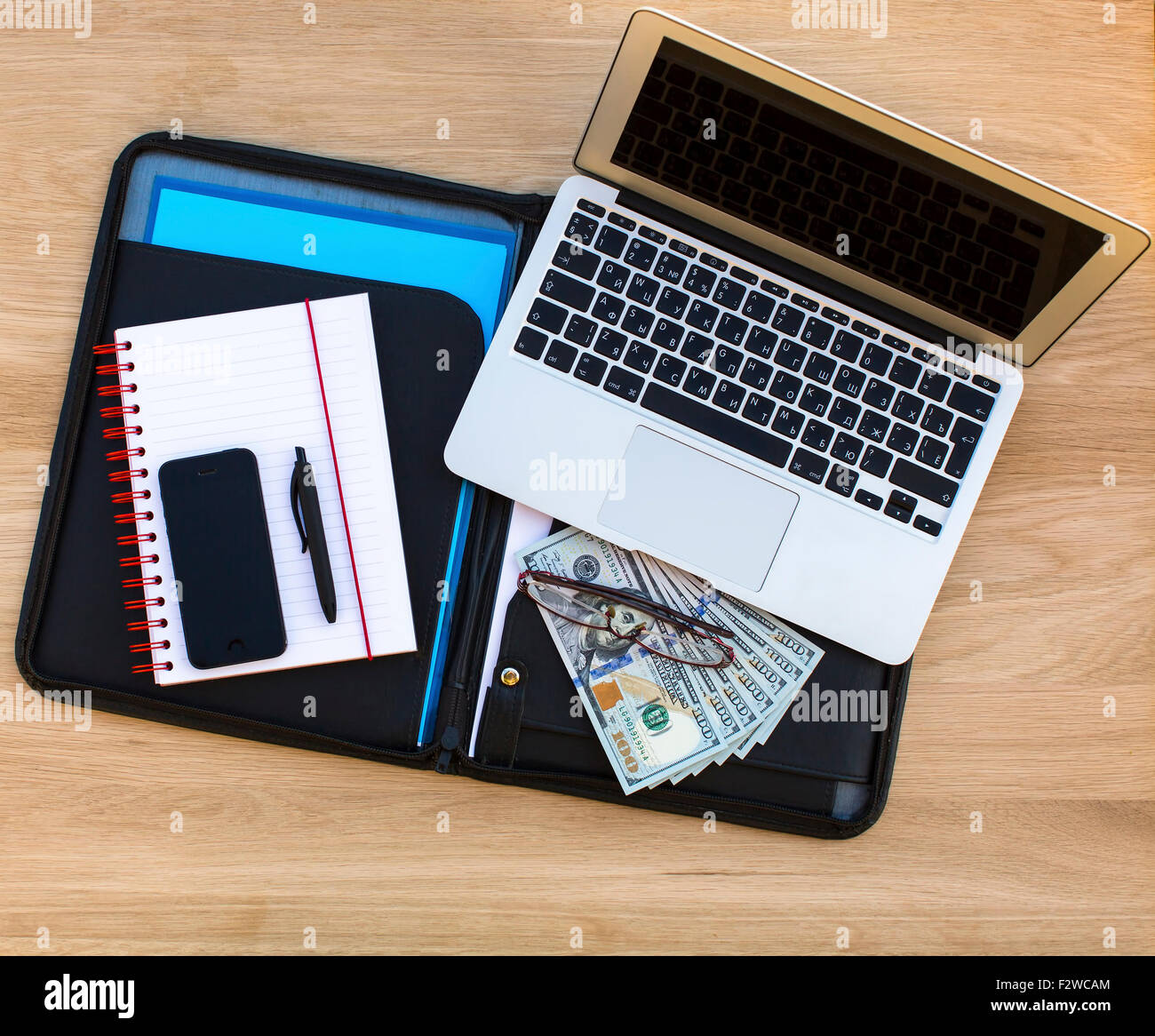 Laptop, Dollarscheine, Brille, Notebook mit einen Stift und ein Smartphone, ein Tablet für Dokumente auf der Holztextur liegen. Stockfoto