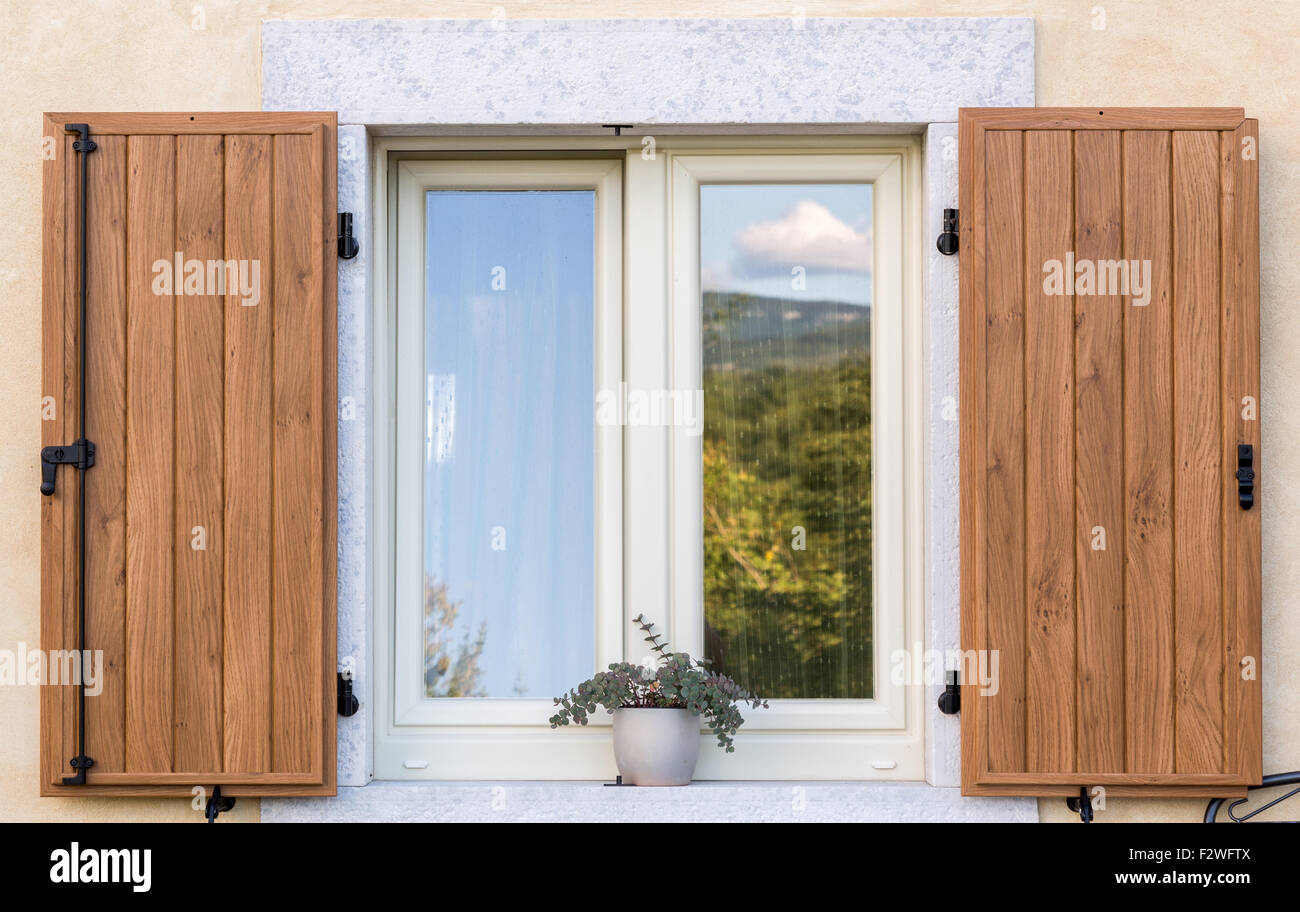 ein schönes Fenster mit offenen braunen Fensterläden aus Holz und Blumen im Topf Stockfoto