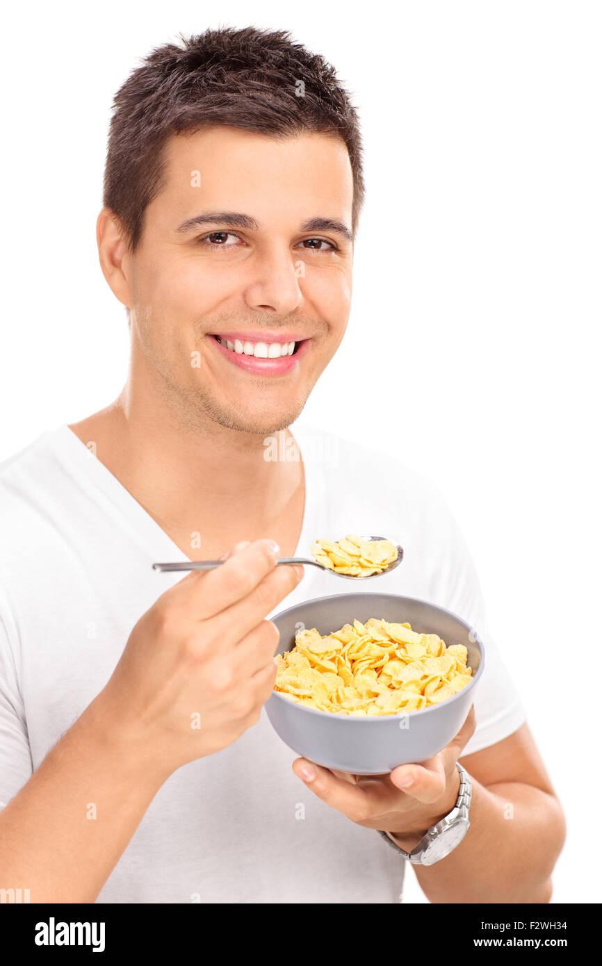 Vertikale Aufnahme eines fröhlichen jungen Mannes Getreide mit einem Löffel aus einer Schüssel Essen und schaut in die Kamera Stockfoto