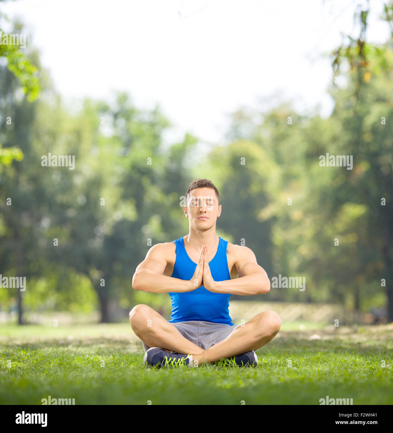 Junge Sportler auf dem Rasen sitzen und meditieren im Park an einem schönen sonnigen Tag mit Tilt-Shift-Objektiv geschossen Stockfoto