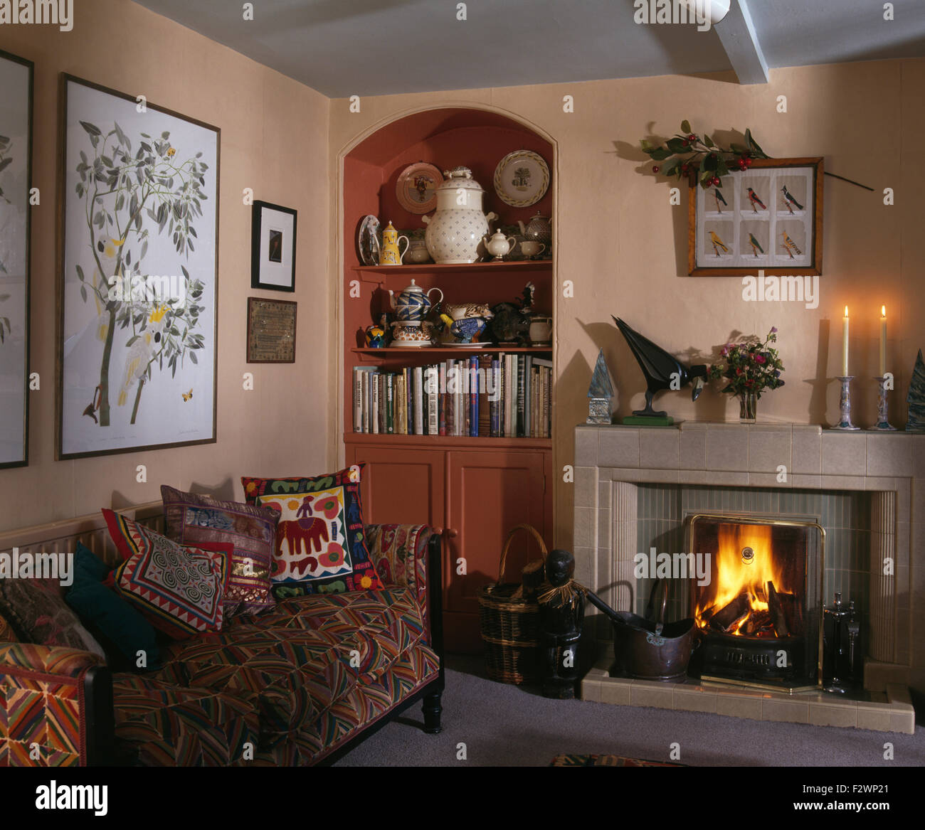 Kamin mit beleuchteten Feuer im Wohnzimmer mit Alkoven Regal- und gemusterten Sofa gestapelt mit ethnischen Kissen der neunziger Jahre Stockfoto