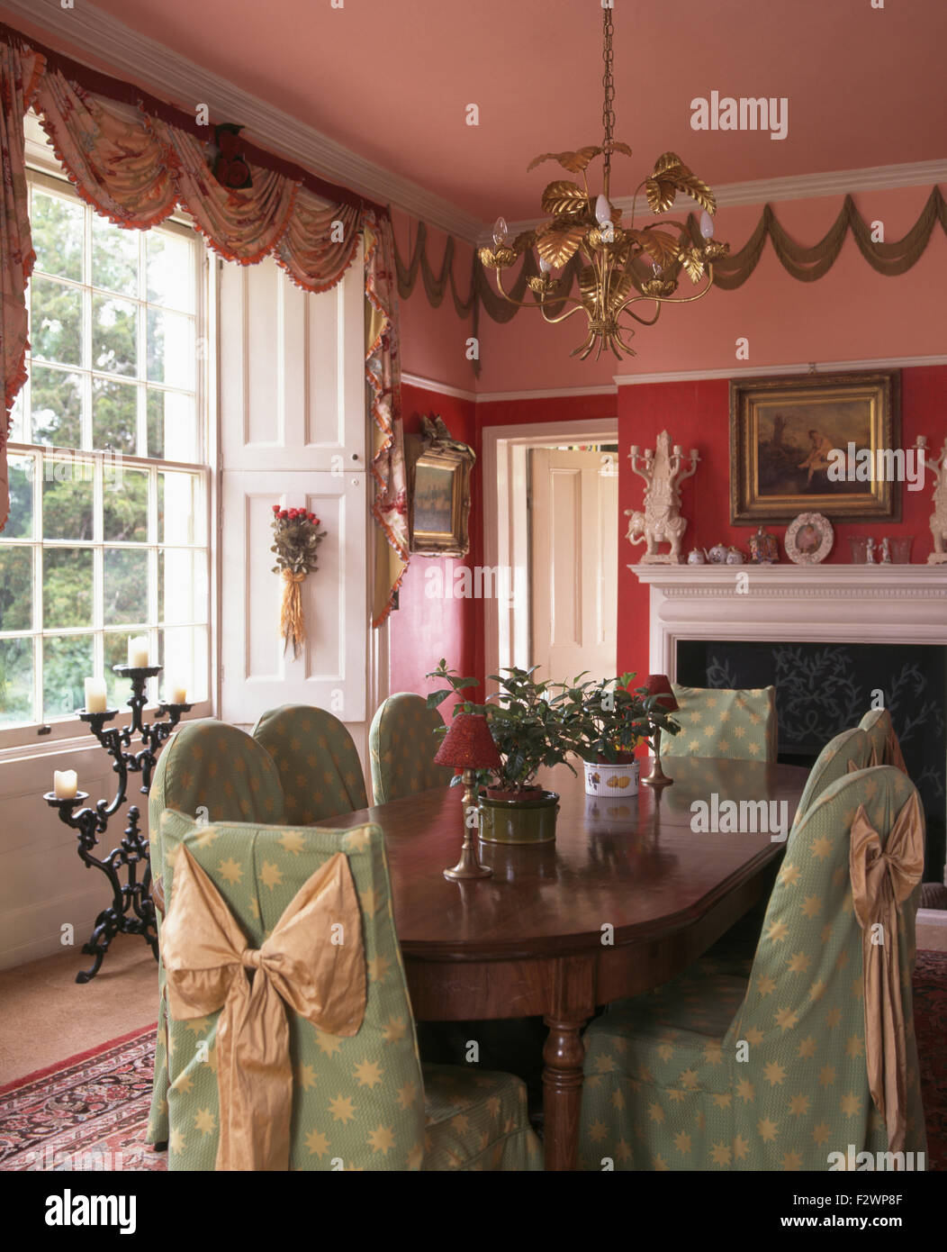 Grüne lose Abdeckungen mit Seide Bögen auf Stühle am Tisch in Rot der neunziger Jahre Esszimmer mit einem Messing Gewicht der Leuchte Stockfoto