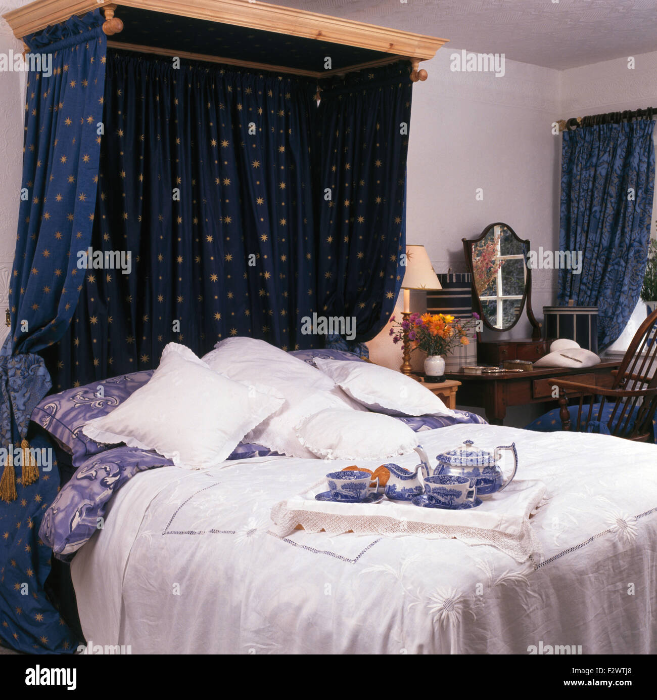 Dunkel blaue Vorhänge auf hölzernen Baldachin über dem Bett mit Frühstückstablett in neunziger Jahre Schlafzimmer Stockfoto