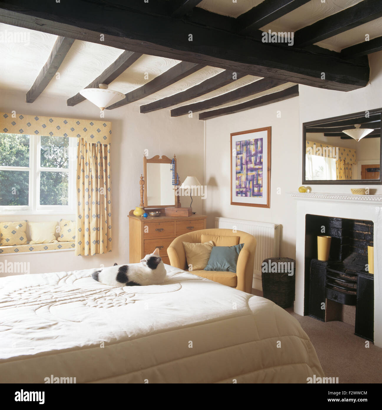 Schwarz + weiße Katze auf auf Bett im Schlafzimmer Ferienhaus mit schwarz bemalten rustikalen Balken und ein Spiegel über dem Kamin Stockfoto