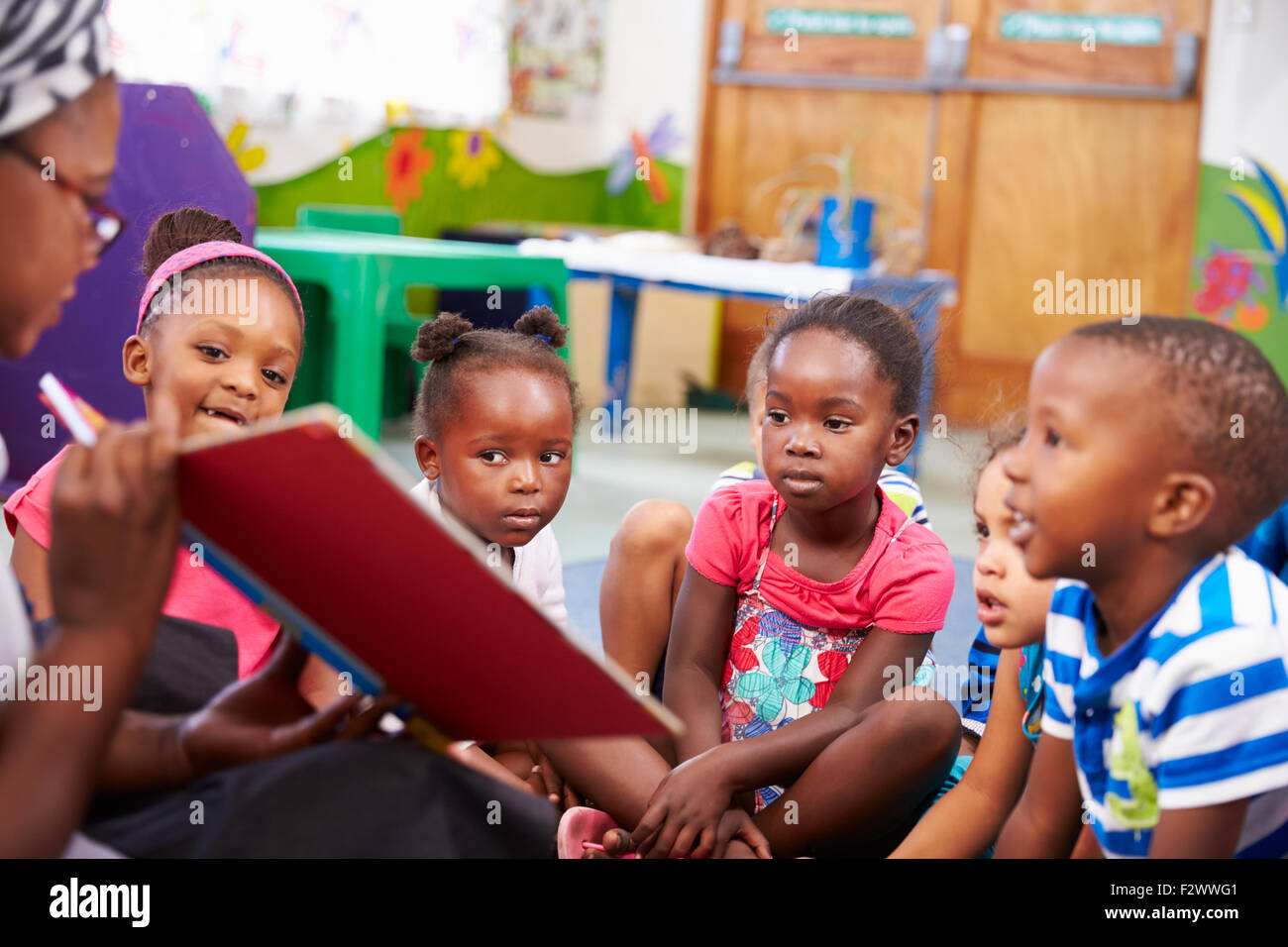 Lehrer, die ein Buch mit einer Klasse von Kindern im Vorschulalter Stockfoto