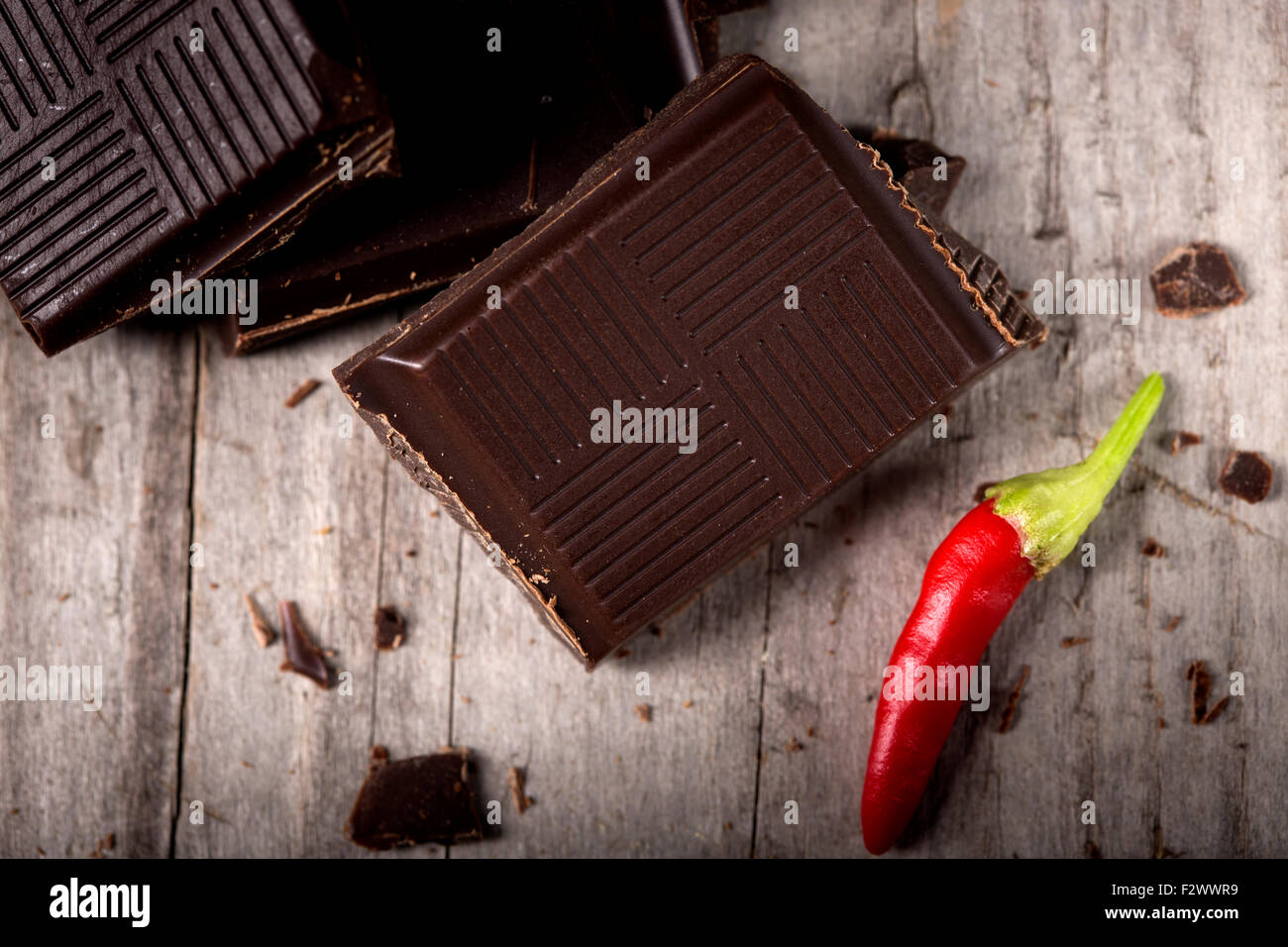 Gehackte Schokolade mit Chili Paprika auf hölzernen Hintergrund Closeup. Stücke von gebrochenen dunkle Schokolade auf Holztisch Makro. Stockfoto