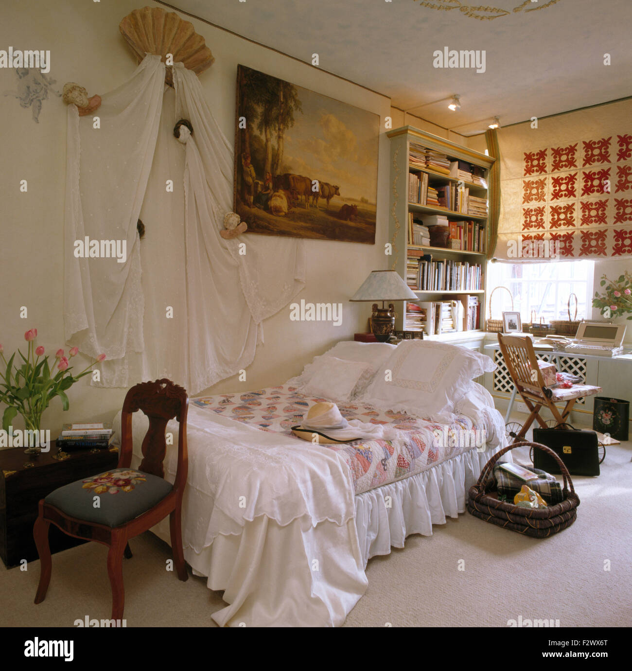 Weiße Vorhänge an Wand über dem Bett mit weißem Leinen und ein Flickenteppich in einem 80er Jahre Wohnung Schlafzimmer Stockfoto