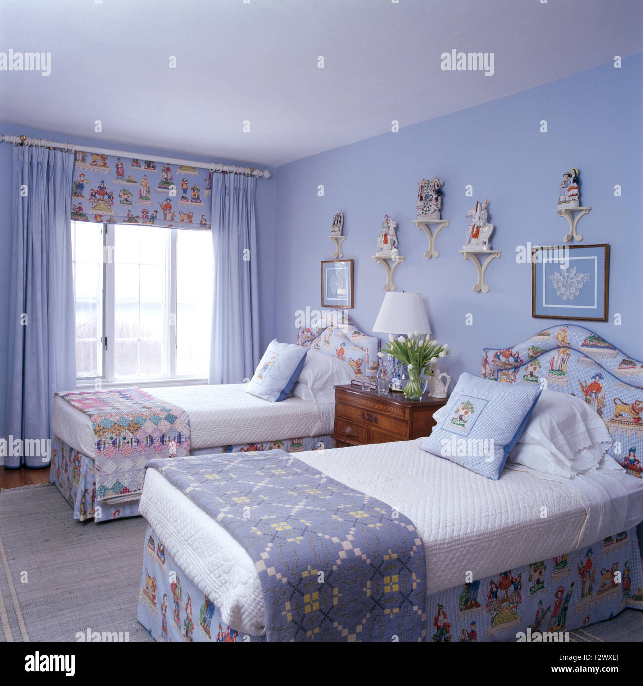 Walisische Decke und einem Patchwork quilt auf Einzelbetten in blassen blauen Schlafzimmer mit blauen Vorhängen und gemusterten blind Stockfoto