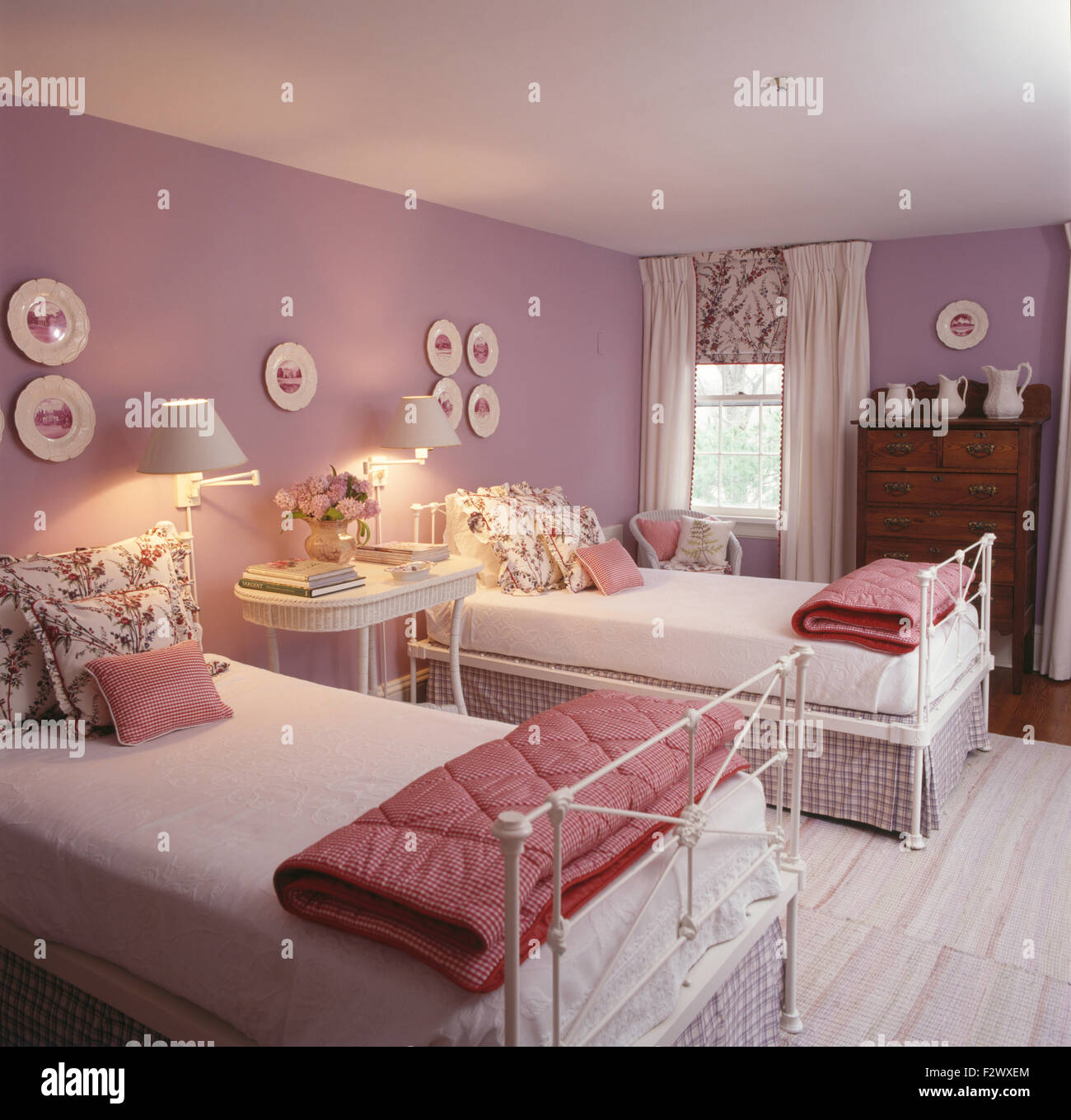 Roten aufgegebenes Duvets und florale Kissen auf weißen Schmiedeeisen Einzelbetten in Mauve neunziger Jahre gefaltet Schlafzimmer Stockfoto