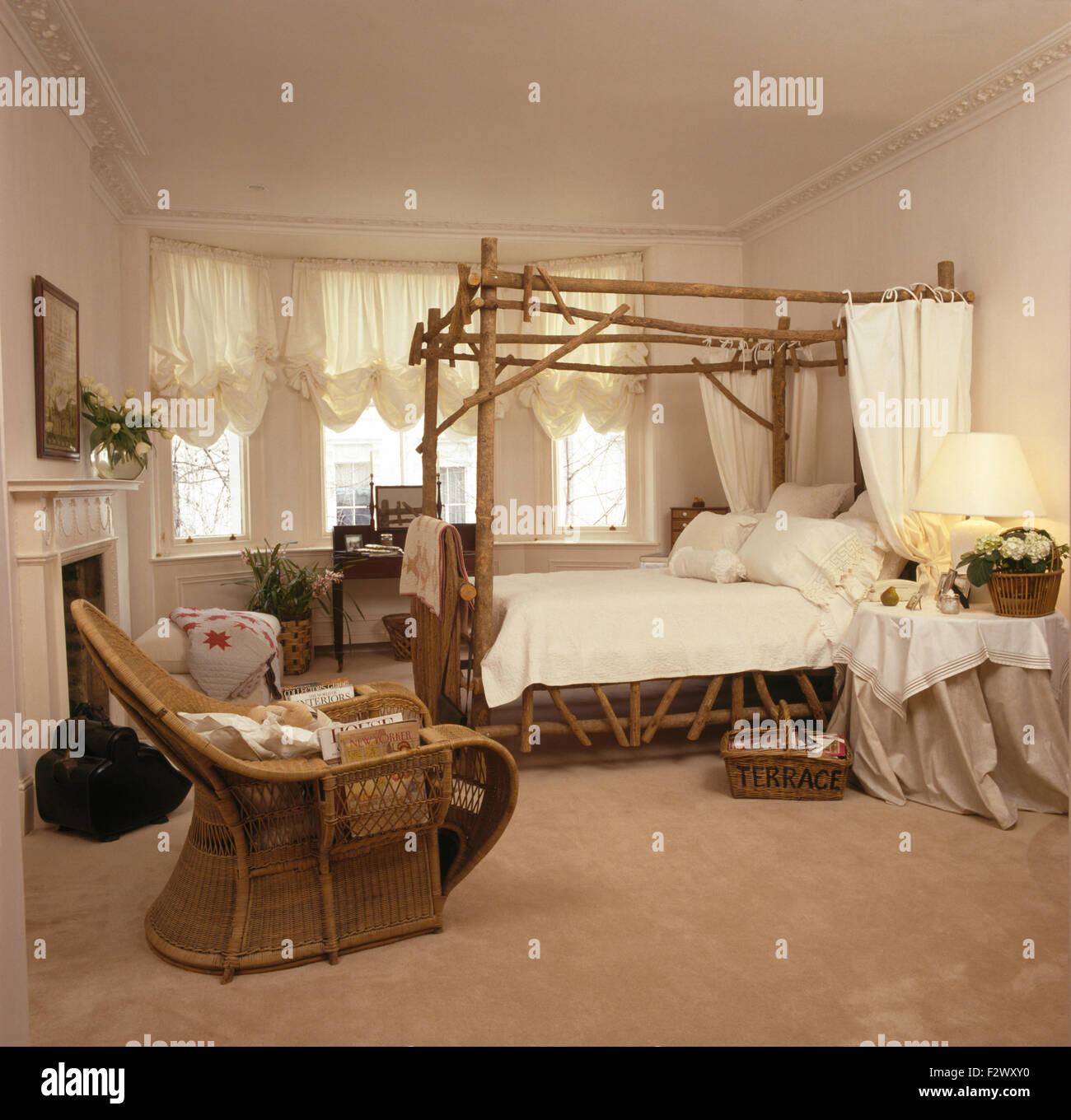 Rohrstock + Peddigrohr Stuhl in neunziger Jahre Schlafzimmer mit rustikalen hölzernen Himmelbett mit weißen Vorhänge und Bettwäsche Stockfoto