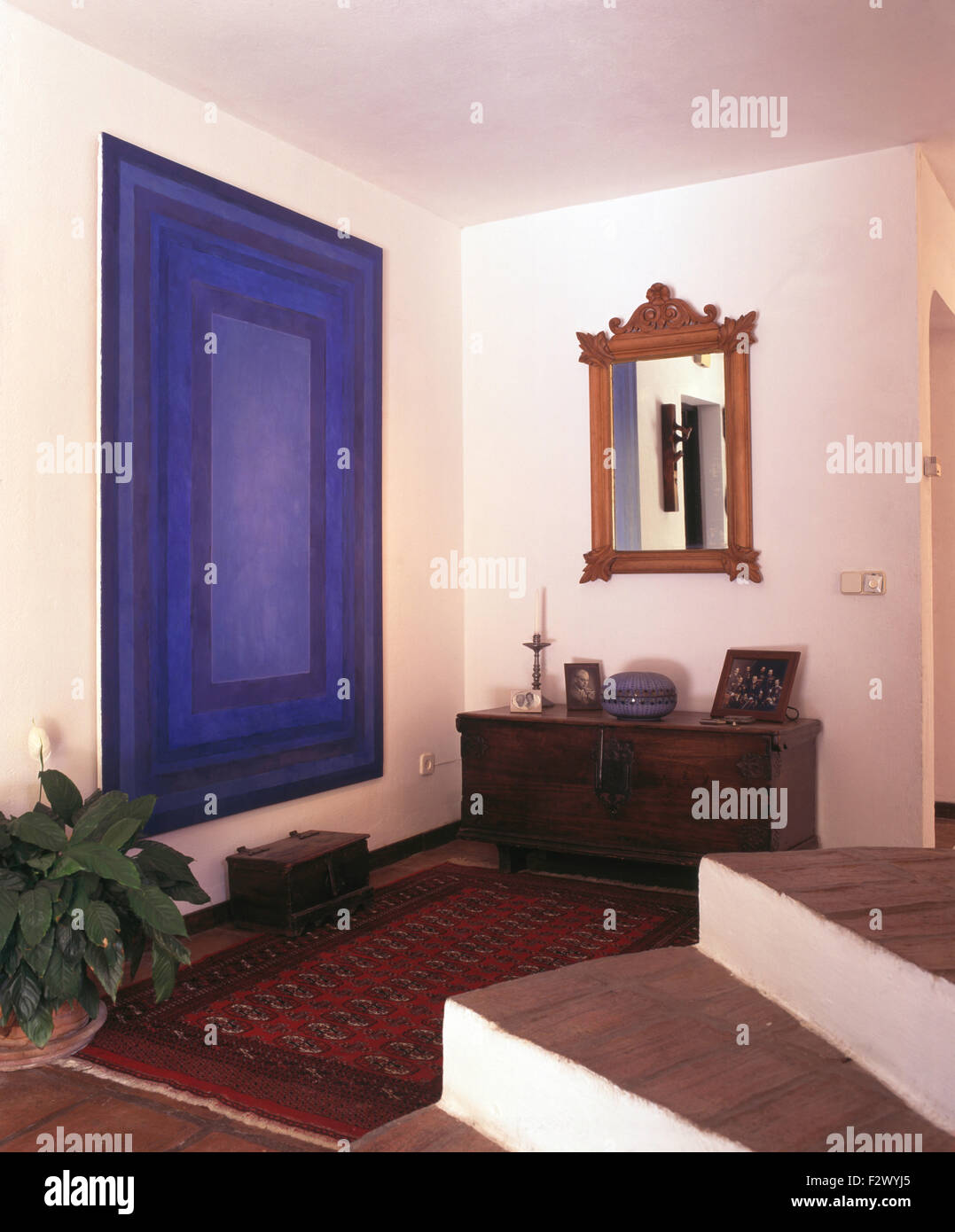 Große blaue abstrakte Malerei und eine orientalische Wolldecke im modernen spanischen Saal mit einem hölzernen Spiegel über eine antike Truhe Stockfoto