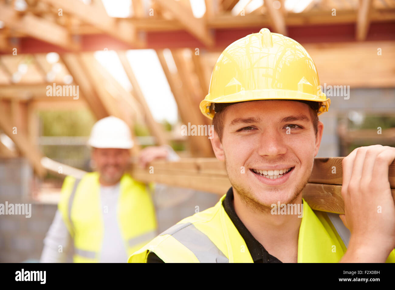 Baumeister und Lehrling trägt Holz auf Baustelle Stockfoto
