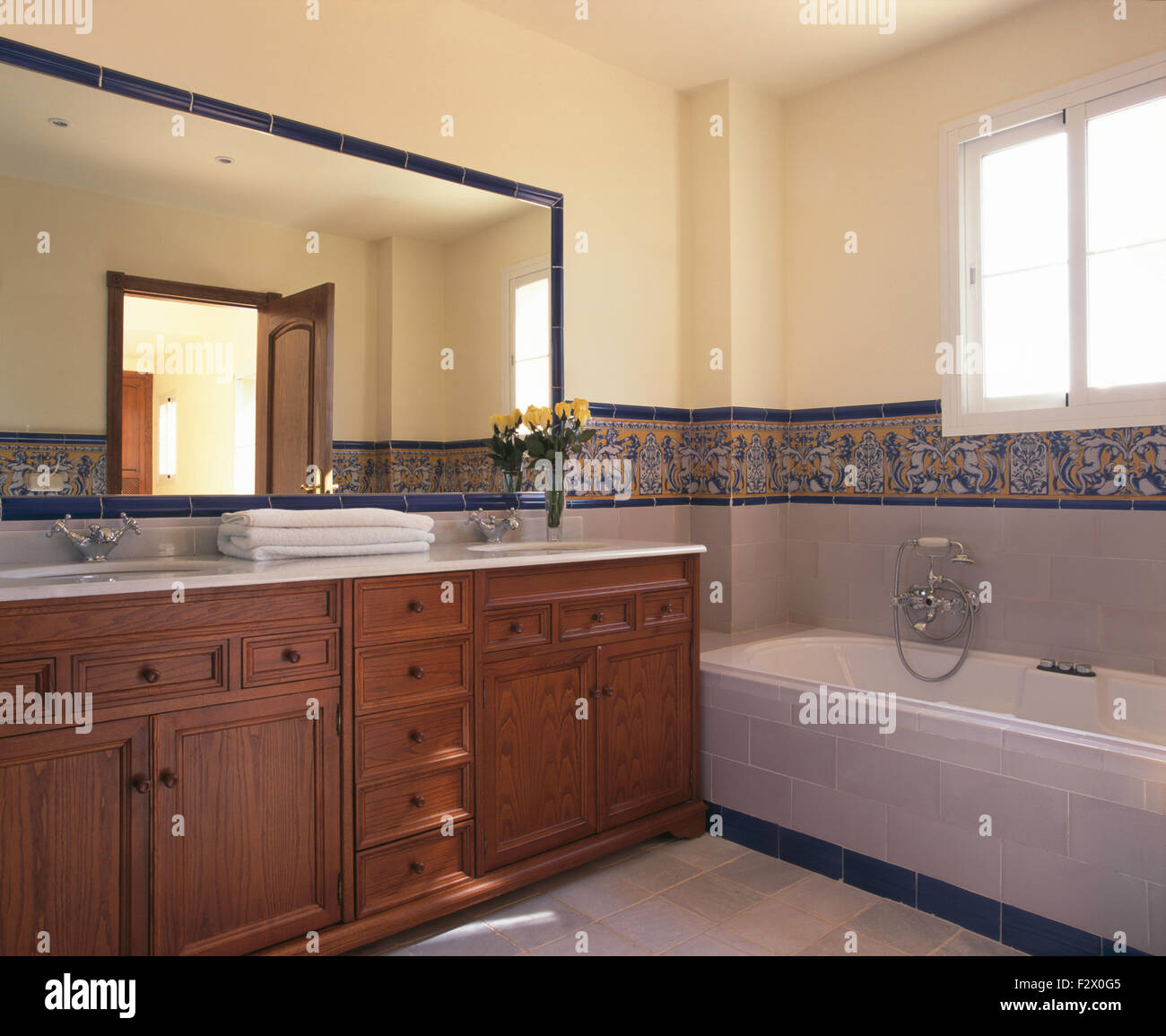 Große Spiegel über hölzerne Waschtischunterbau in modernen spanischen Badezimmer mit einem gefliesten Rand über der Badewanne Stockfoto
