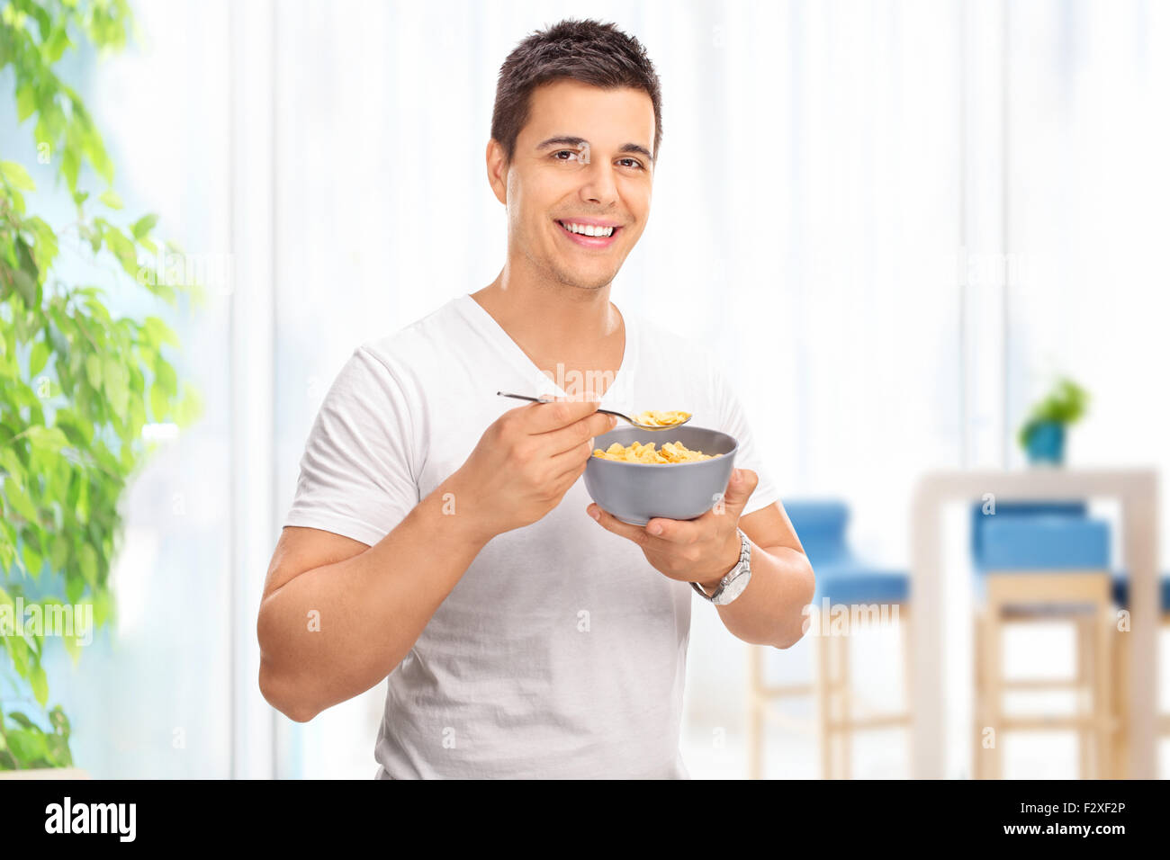 Junger fröhlicher Mensch Getreide aus einer Schüssel Essen und schaut in die Kamera zu Hause Stockfoto