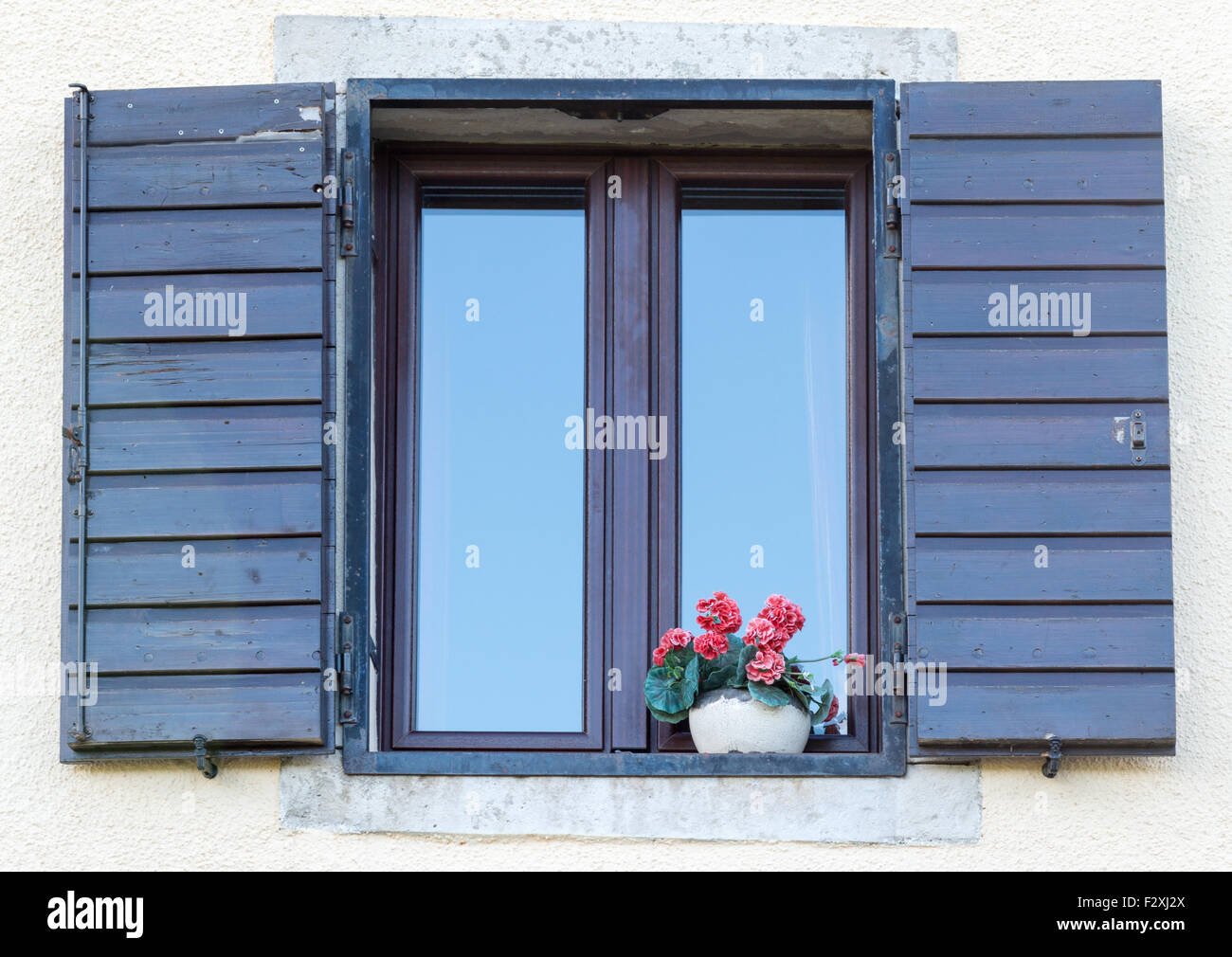 ein schönes Fenster mit offenen braunen Fensterläden aus Holz und Blumen im Topf Stockfoto