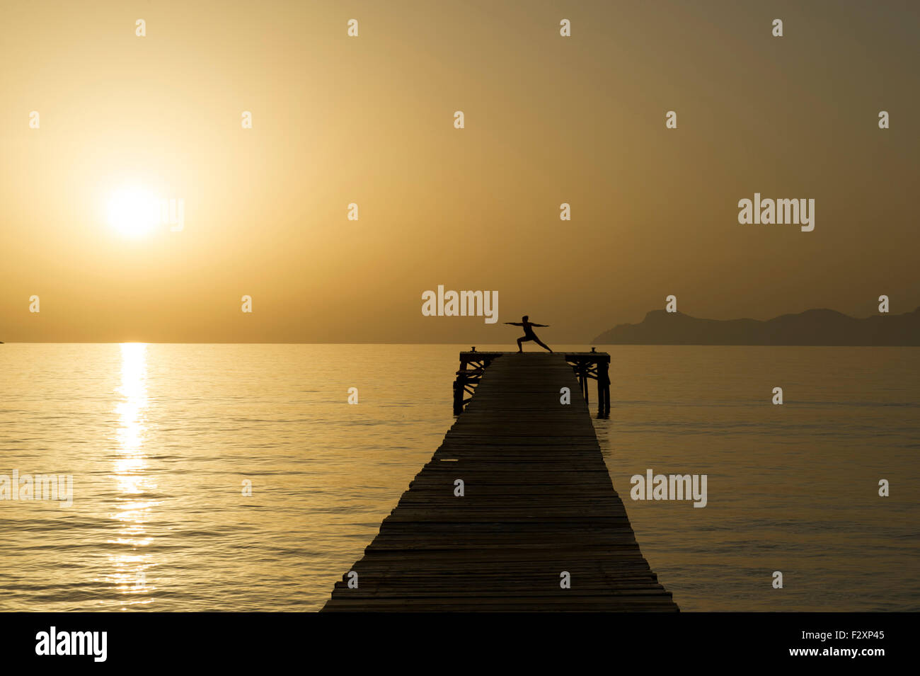 Eine junge Frau praktizieren Yoga auf dem Steg bei Sonnenaufgang im Hafen d'Alcudia, Mallorca Stockfoto