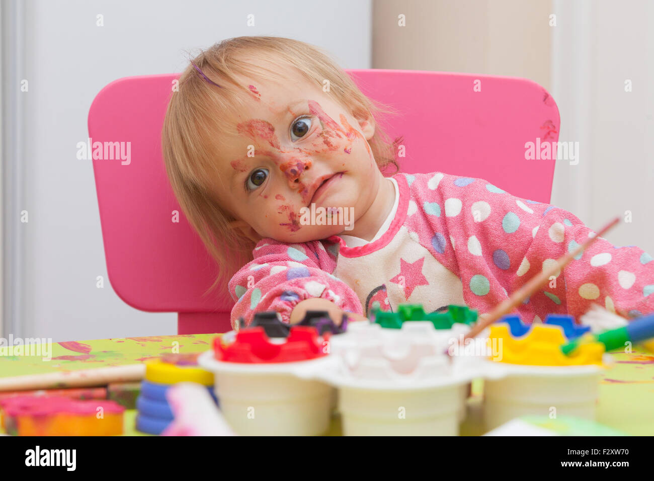 Ein 16 Monate alt, Blond Haare, Bürsten kaukasisch, Mädchen spielen mit Farben und die Farbe während des Sitzens im Inneren an einem kleinen Tisch. Stockfoto