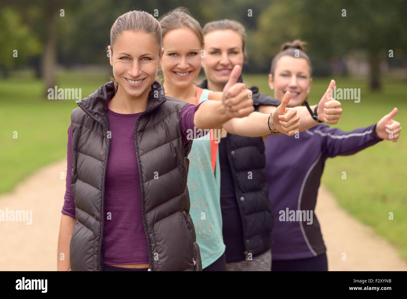 Vier glückliche gesunde Jungen Damen in Linie, zeigt Daumen nach oben auf die Kamera nach ihrer Bewegung im Freien. Stockfoto