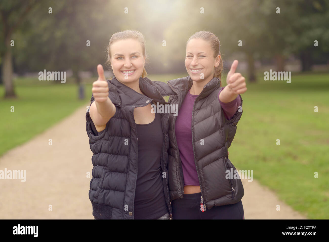 Halbe Körper Schuss von zwei glückliche gesunde Frau an den Park zeigt Daumen nach oben auf die Kamera nach ihrer Ausbildung. Stockfoto