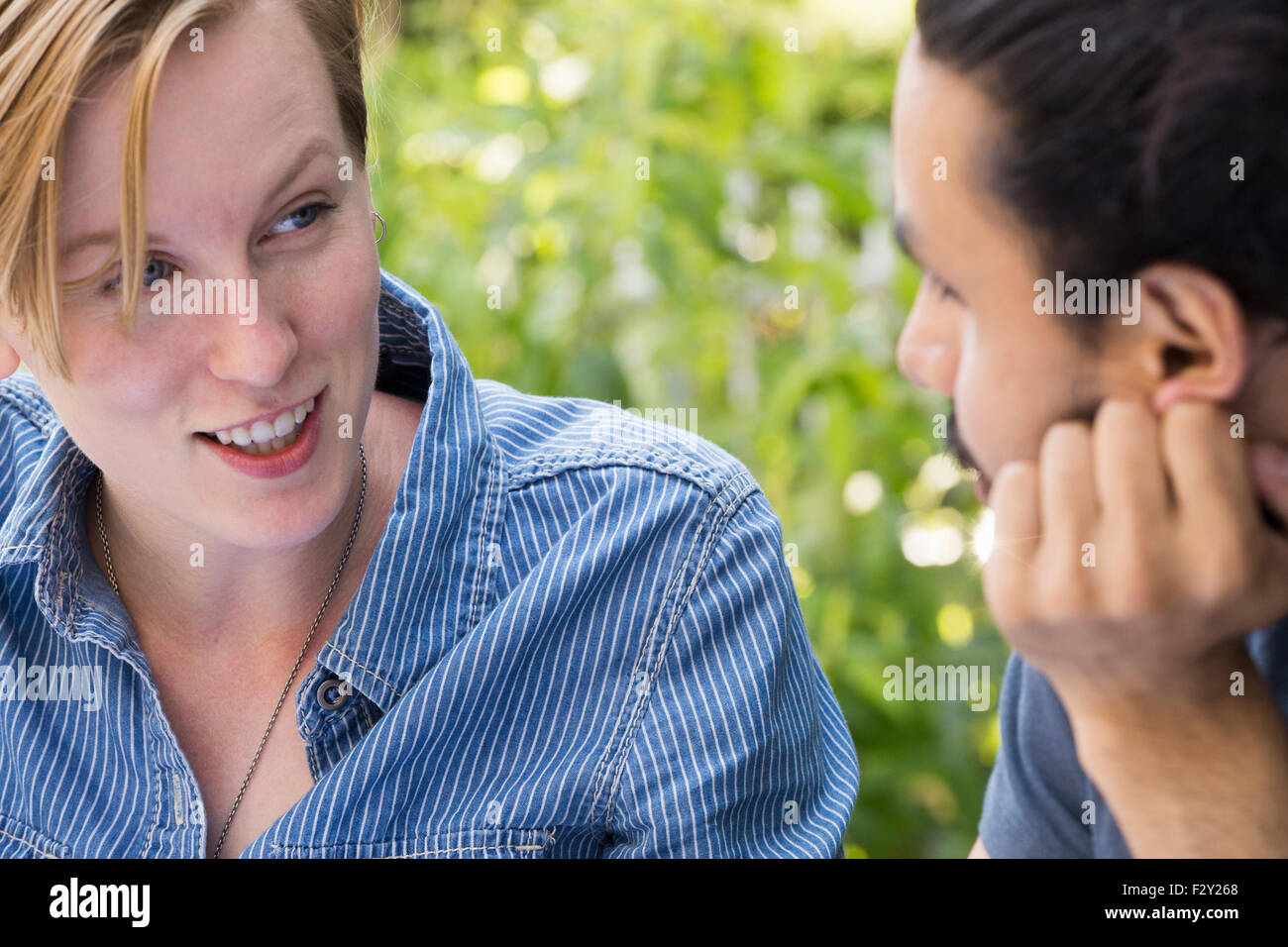 Nahaufnahme der ein junger Mann und eine Frau sitzen nebeneinander, lächelnd und reden. Stockfoto