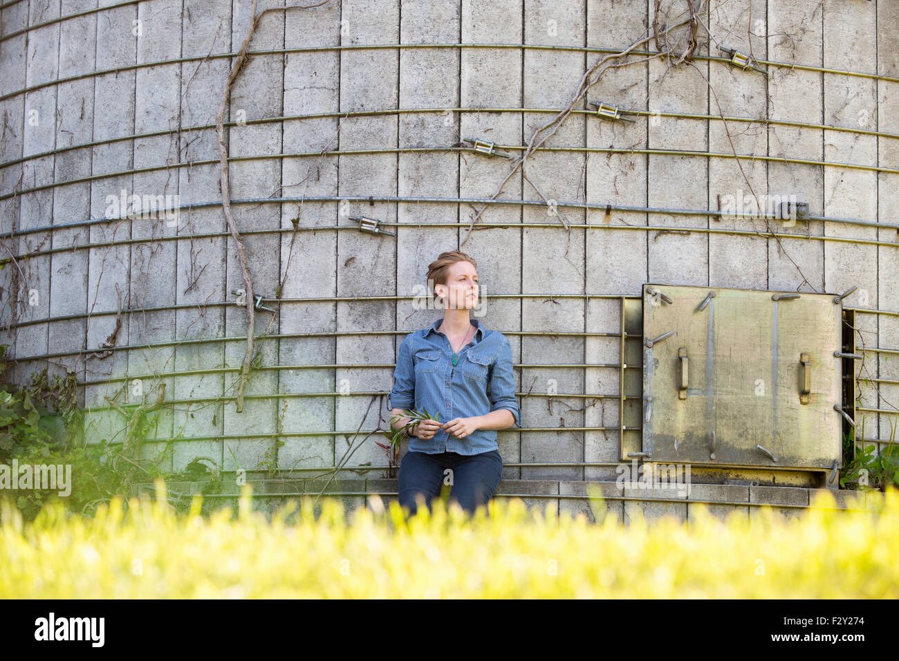 Junge Frau auf einem bewirtschafteten Bauernhof, eine Pause im Schatten eines Silos. Stockfoto