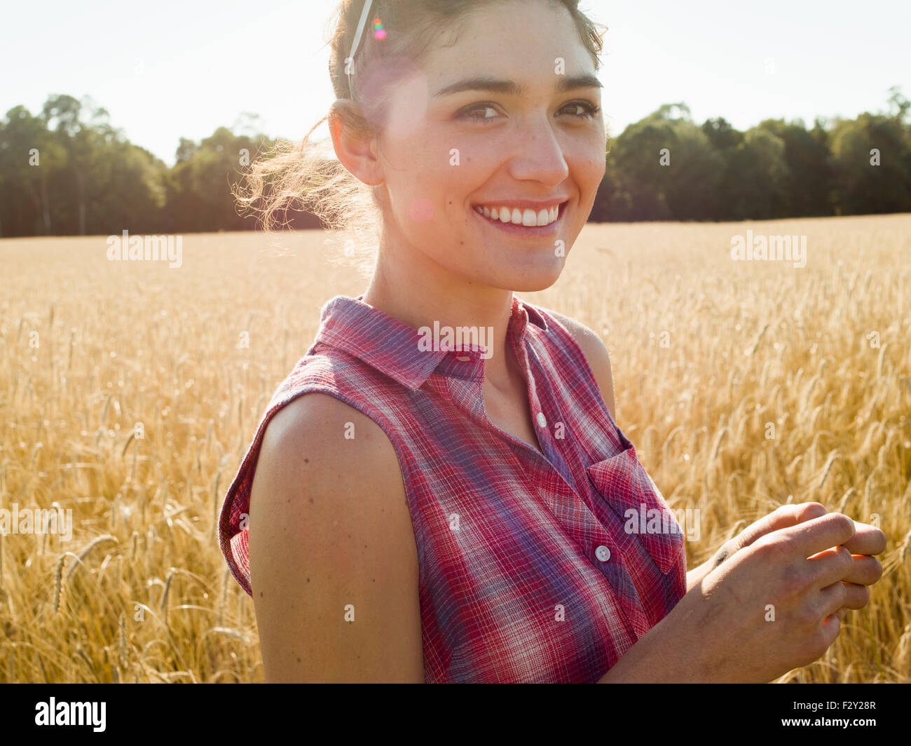 Lächelnde junge Frau trägt ein kariertes Hemd steht in einem Maisfeld. Stockfoto