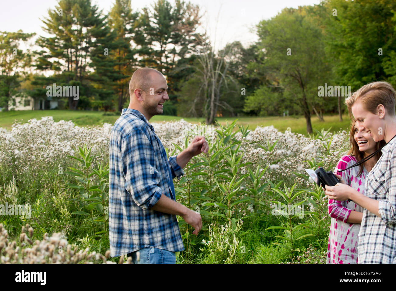 Drei Menschen, ein Mann und zwei Frauen in einer Wildblumenwiese stehen. Eine Frau hält eine Kamera mit Birne Flash-Anlage. Stockfoto
