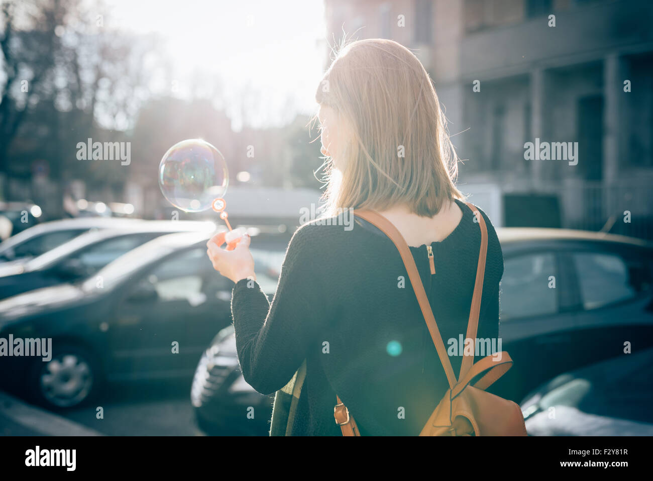 Halbe Länge Blick von hinten junge schöne Hipster sportliche blonde Frau in der Stadt spielen mit Blase Seife - Kindheit, Glück, Sorglosigkeit Konzept - Hintergrundbeleuchtung Stockfoto