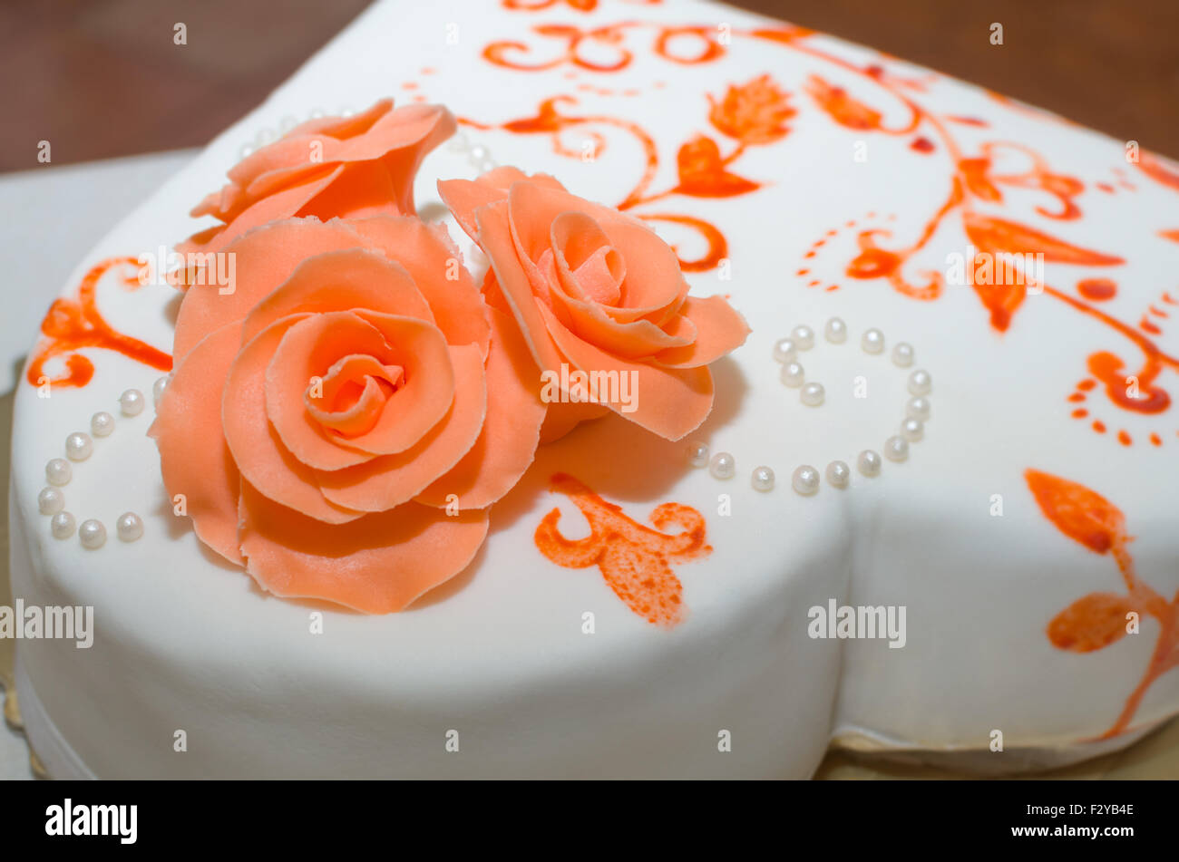 Herzförmige weiße Hochzeitstorte mit orangefarbenen Rosen und Perlen Dekoration Nahaufnahme Stockfoto