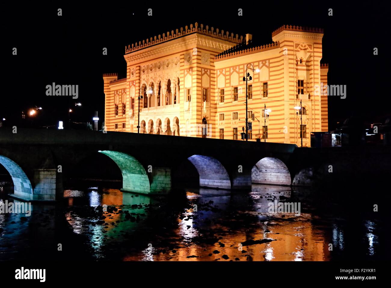 Nationale Bibliothek von Bosnien und Herzegowina und Fluss Miljacka in Sarajevo in der Nacht. Stockfoto