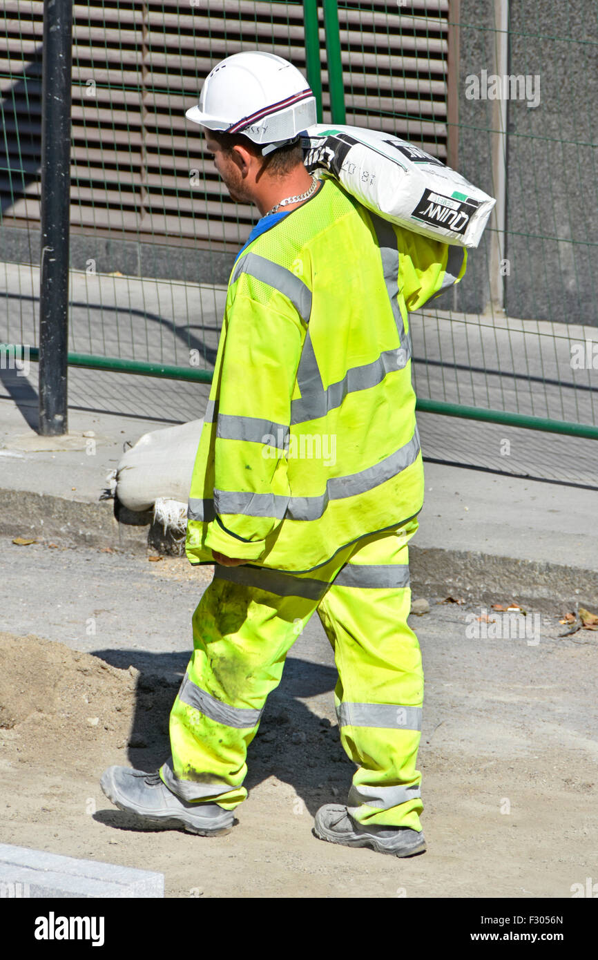 Arbeiter, die ein Sack Zement auf seiner Schulter tragen hohe Sichtbarkeit Health & Safety Jacket auf einer Fahrbahn Konstruktion Ort London England Großbritannien Stockfoto