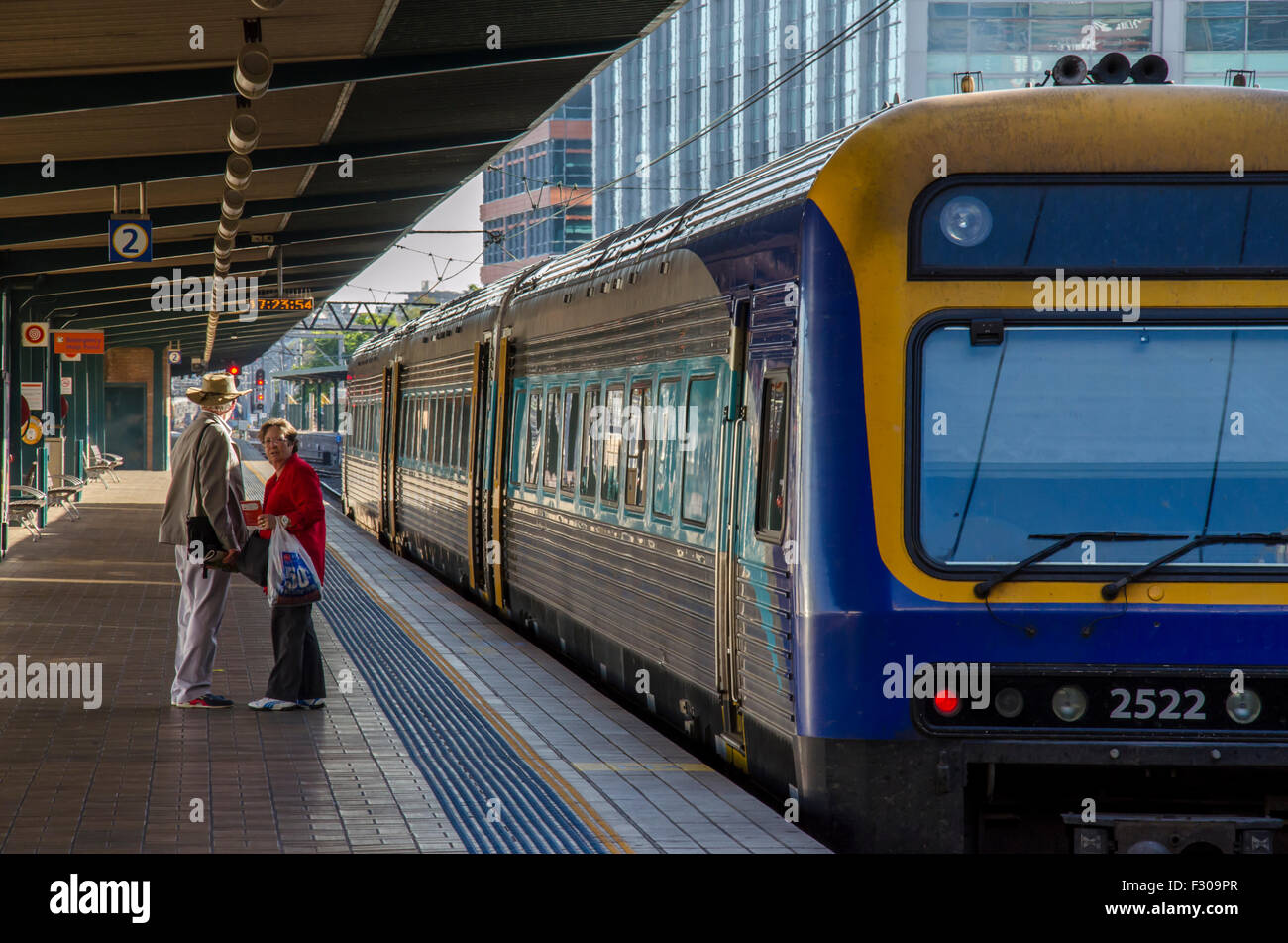 Zwei ältere Menschen warten auf einem Bahnsteig neben einem wartenden Zug. Der Zug ist ein Diesel Endeavour Klasse Lokomotive Land Service aus Sydney. Stockfoto