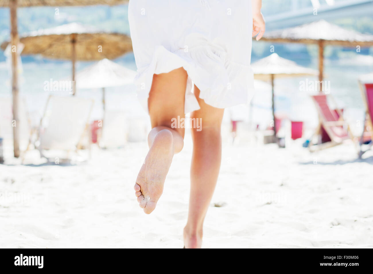 Frau im weißen Sommer Kleid laufen am Sandstrand unter den Liegestühlen und Sonnenschirmen, Sicht nach hinten. Stockfoto