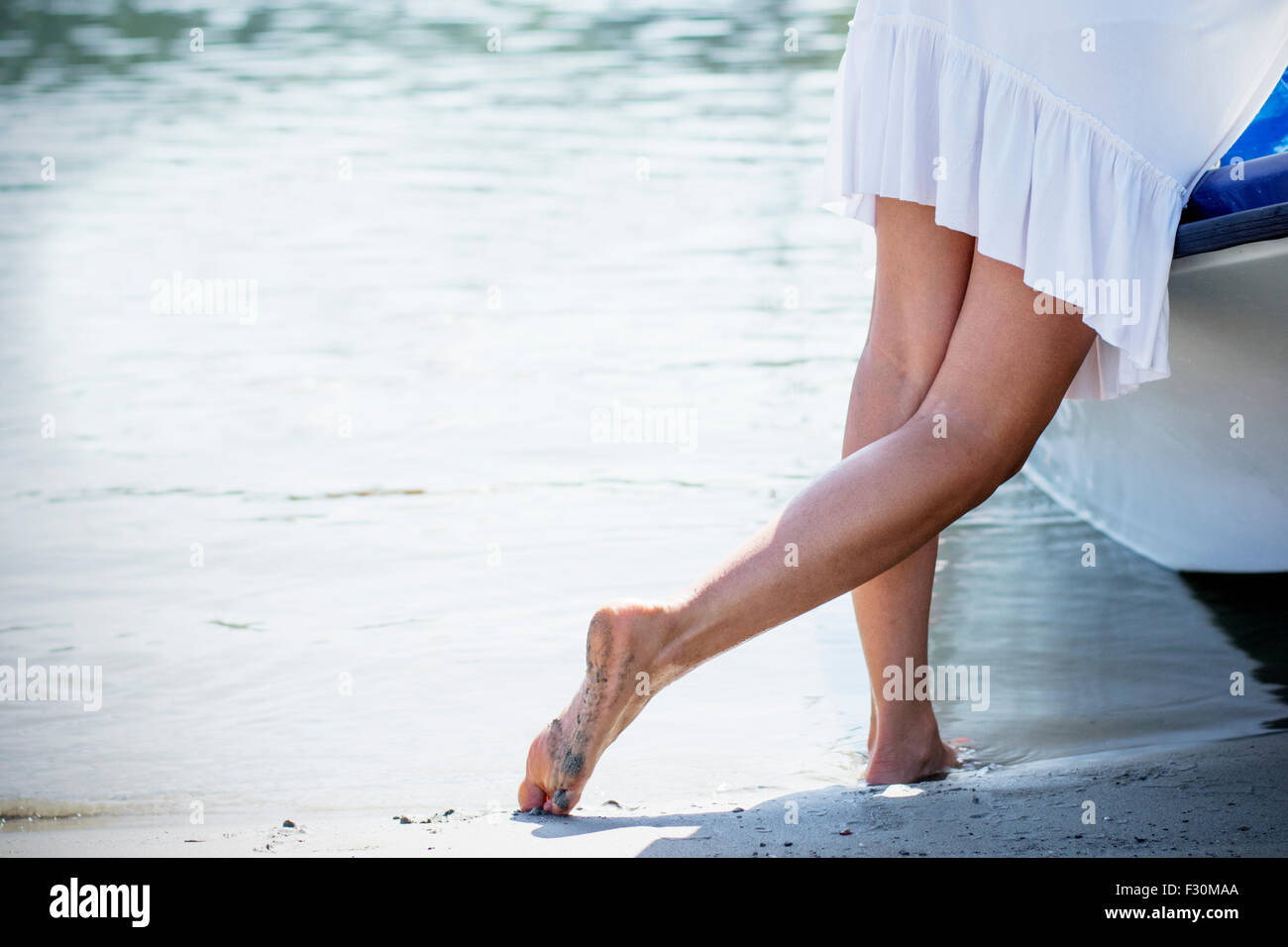 Frau im weißen Sommerkleid am Sandstrand stützte sich auf kleinen Boot. Stockfoto