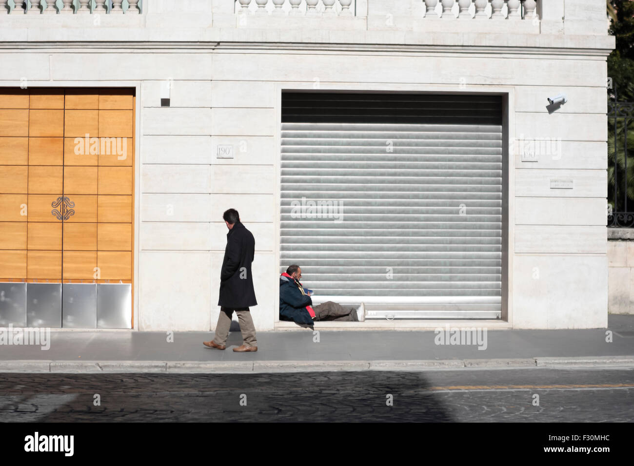 Obdachlos in Rom. Ein Obdachloser sitzt in einer Ladentür und zieht die Aufmerksamkeit eines Passanten auf sich. Via Nazionale, Rom, Italien. Stockfoto