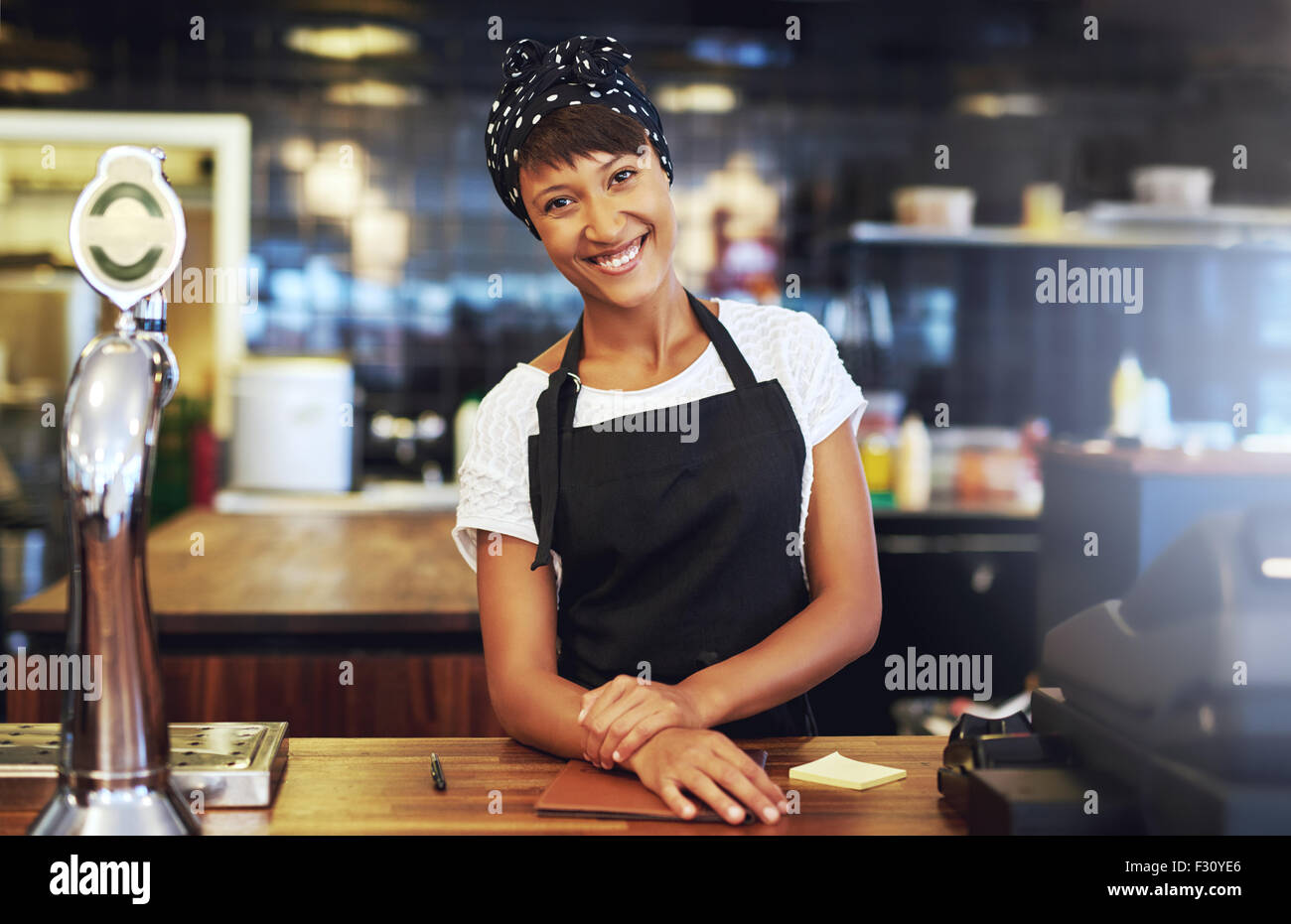 Warme einladende junge Unternehmen Unternehmer stehen hinter der Theke in ihrem Café geben der Kamera ein strahlendes Lächeln willkommen Stockfoto
