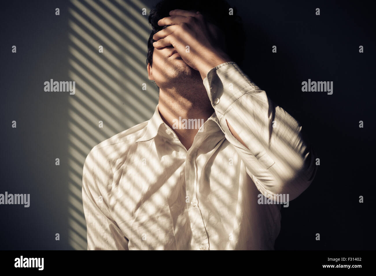 Junger Mann neben einem Fenster mit Schatten von den blinds Stockfoto