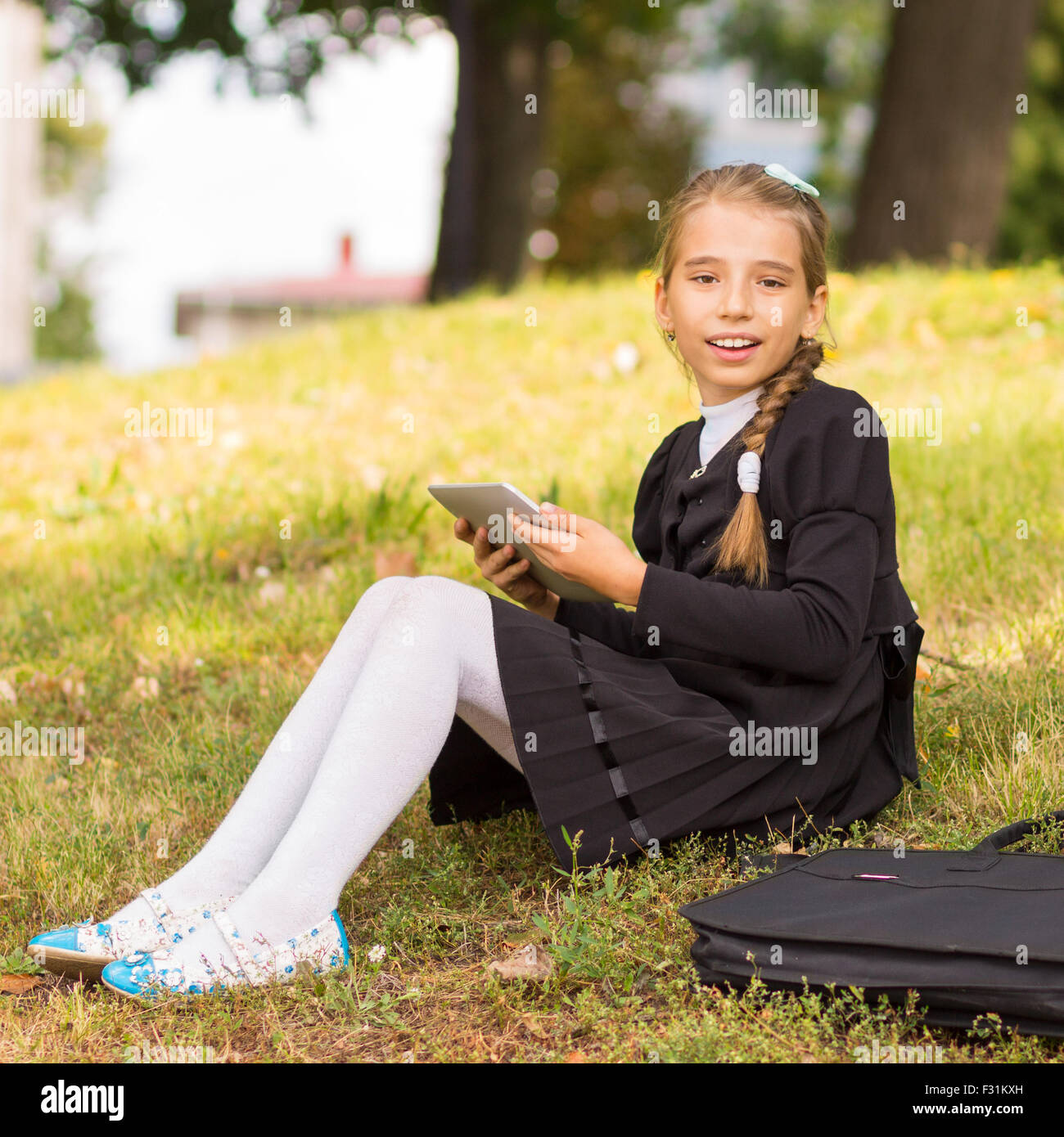 Kleine Studentin auf dem Rasen sitzen und mit Tablet-PC. Lächelnd Schüler Rest nach der Schule im Park im Freien. Stockfoto