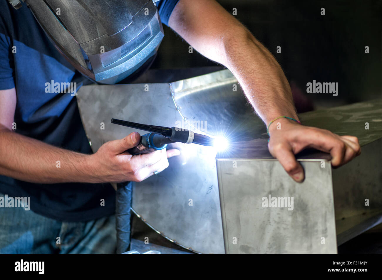 Schlosser Schweißen zwei Metallkomponenten mit einer industriellen Schweißer in einer Werkstatt, Dreh Winkel Nahaufnahme seiner Hände Stockfoto