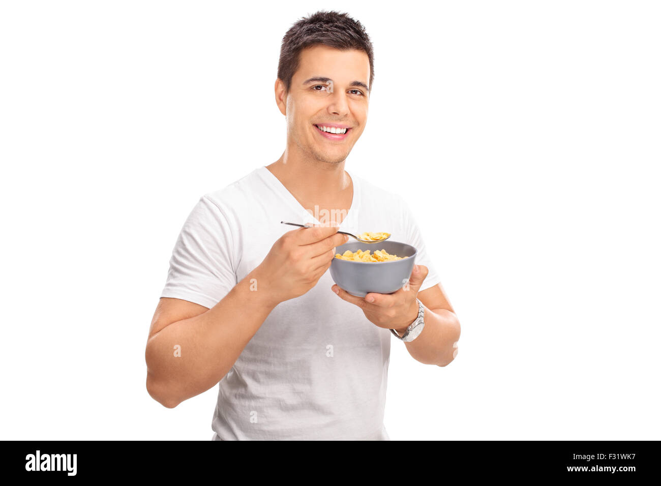Fröhlicher junge Mensch Getreide aus einer Schüssel Essen und schaut in die Kamera, die isoliert auf weißem Hintergrund Stockfoto